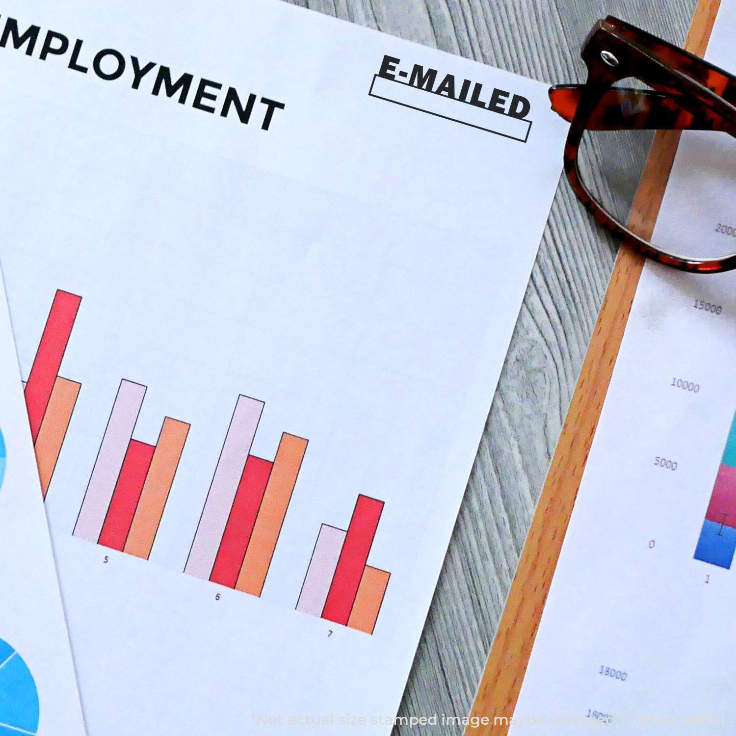 E-mailed with Date Box Rubber Stamp used on a document with charts and graphs, next to eyeglasses on a wooden surface.