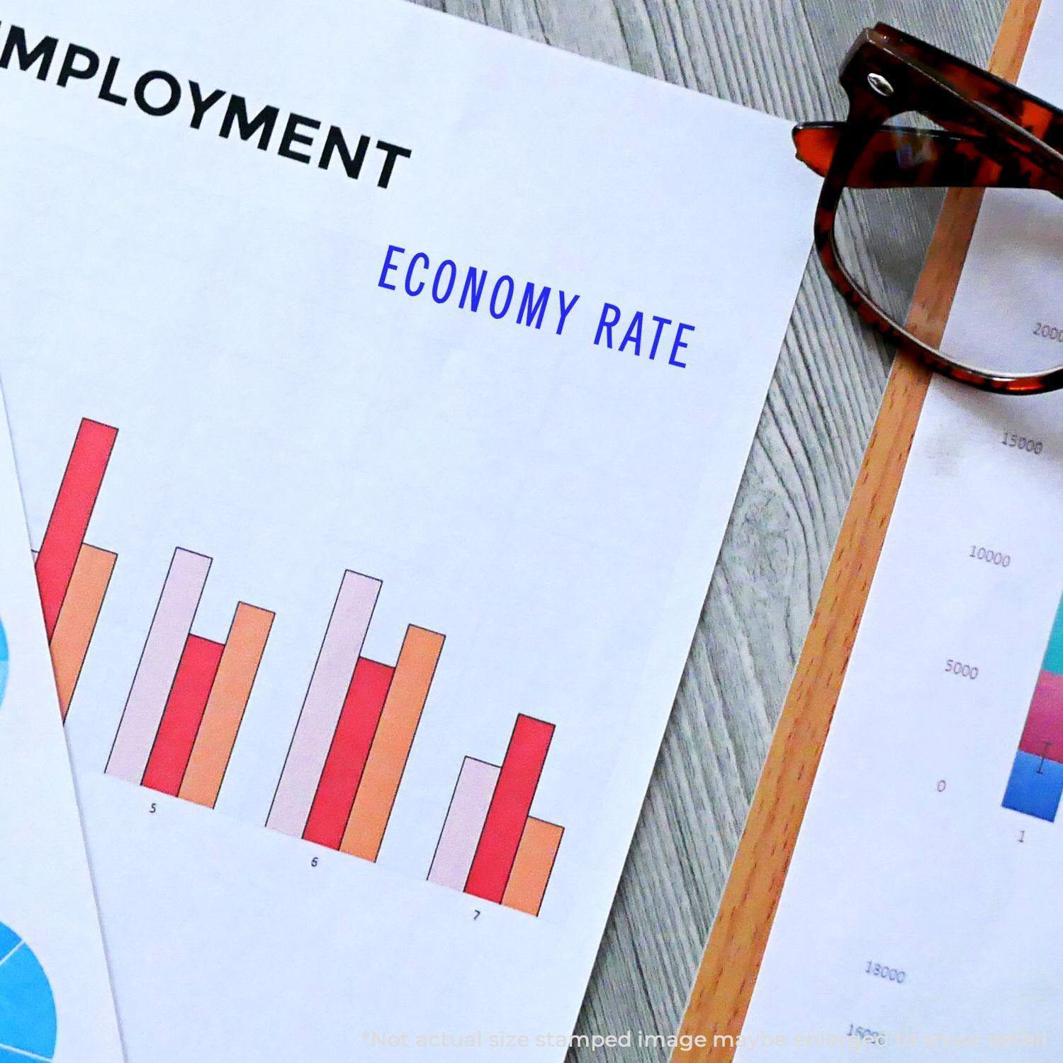 Self Inking Economy Rate Stamp used on a document with employment graphs and charts, next to a pair of glasses on a wooden desk.