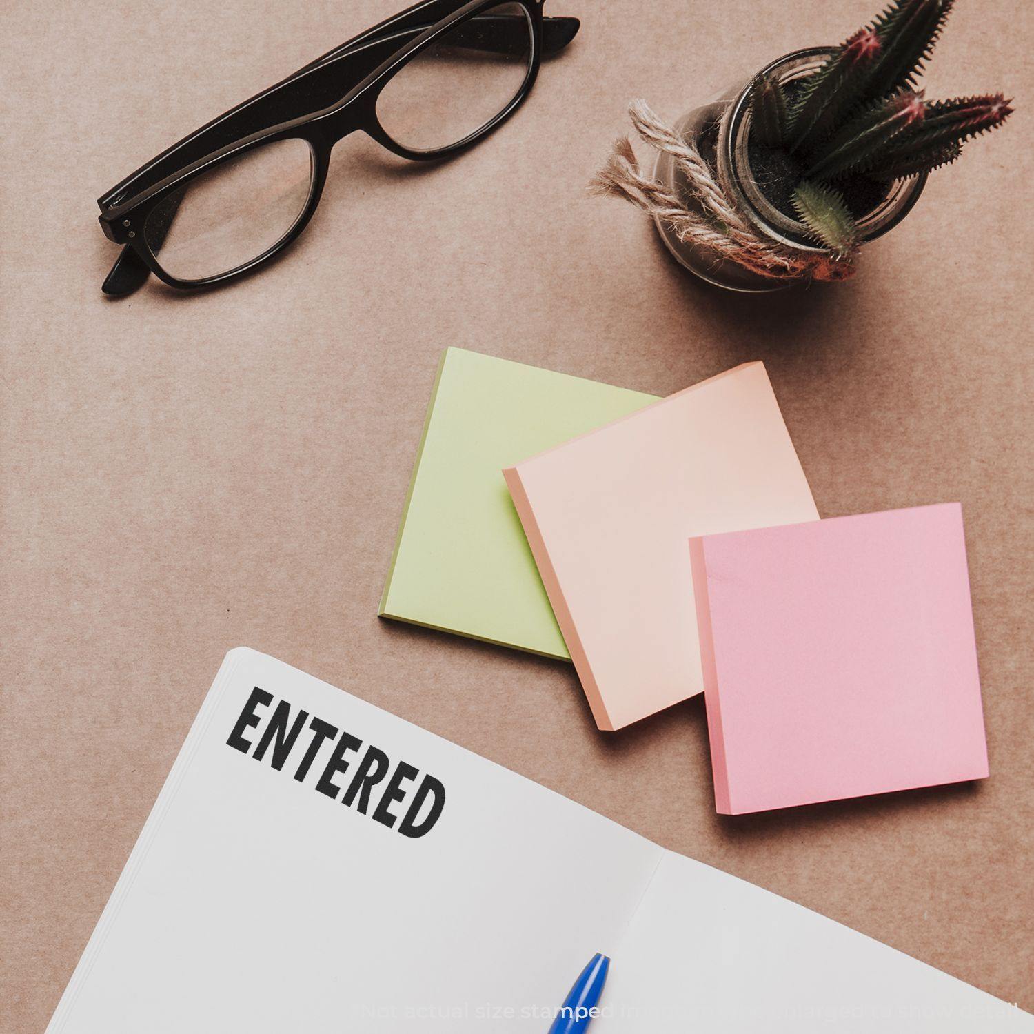 Large Pre-Inked Entered Stamp used on a document, with glasses, sticky notes, and a plant on a desk.