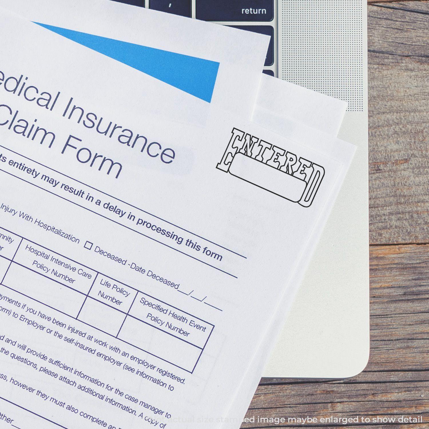 Large Pre-Inked Entered with Date Box Stamp marking ENTERED on a medical insurance claim form placed on a laptop keyboard.