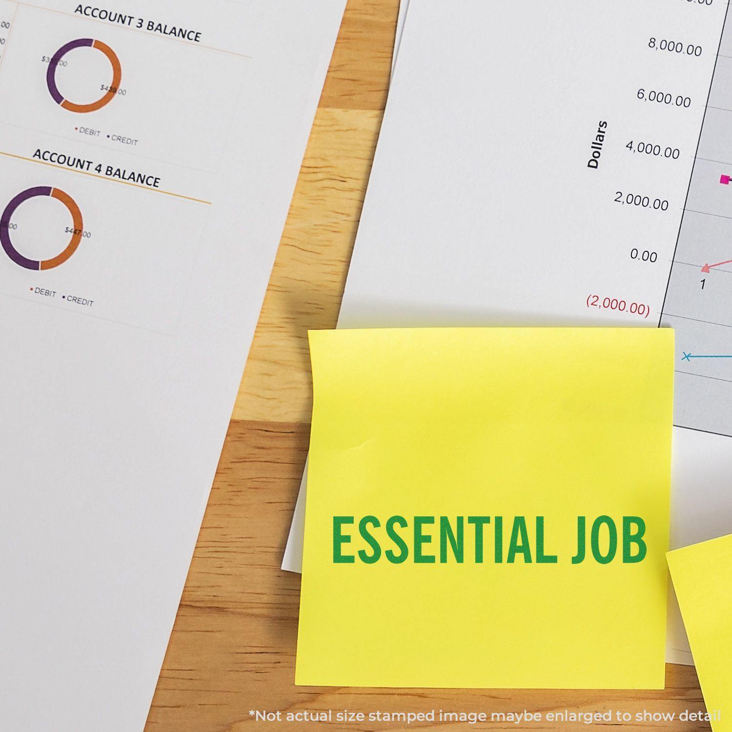 Large Pre-Inked Essential Job Stamp used on a yellow sticky note, placed on a desk with financial documents and charts.