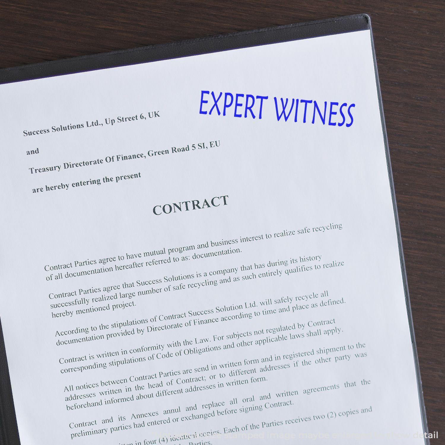 A Self Inking Expert Witness Stamp marks a contract document with EXPERT WITNESS in blue ink, highlighting its use in legal contexts.