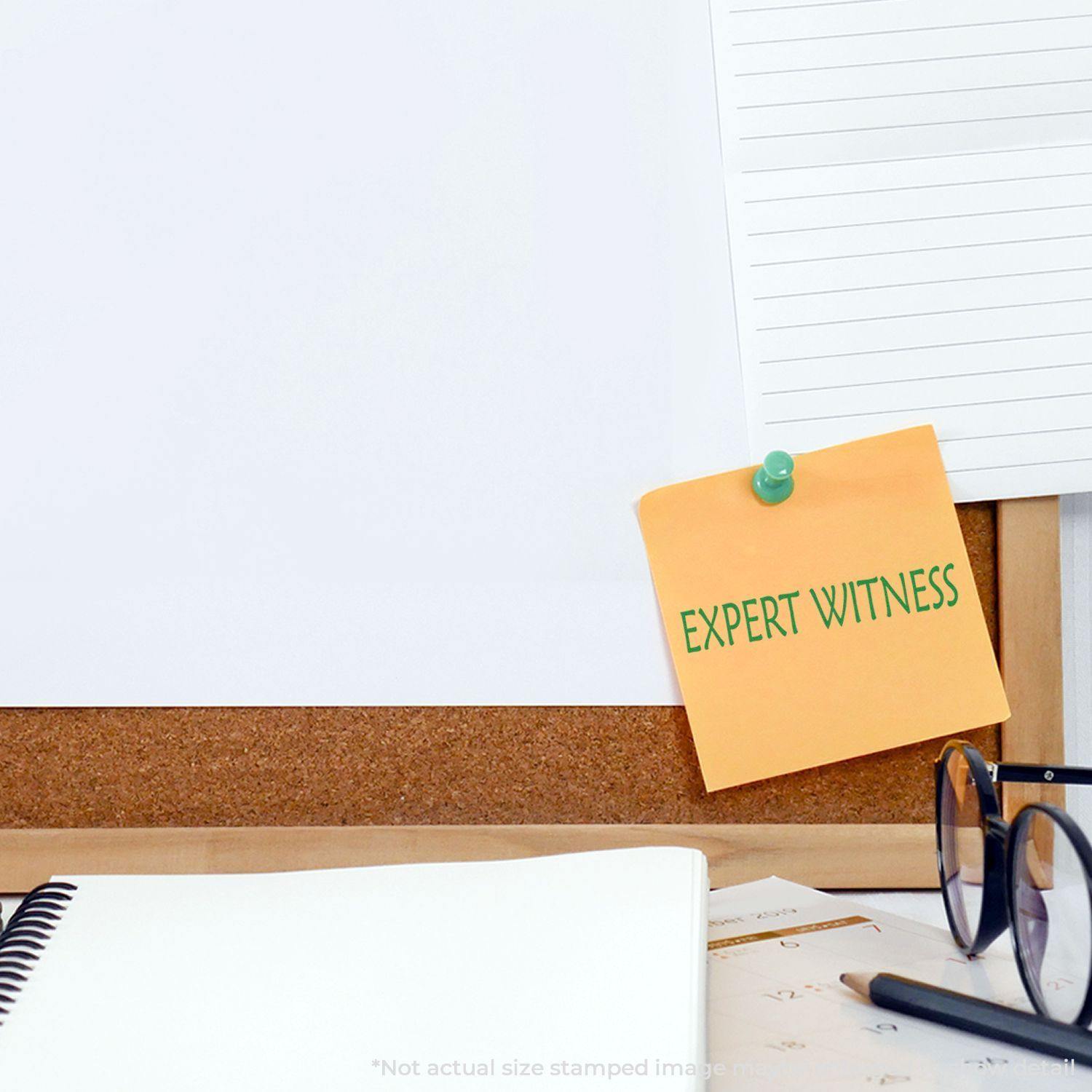 Expert Witness Rubber Stamp used on a yellow sticky note pinned to a corkboard, with a notebook, glasses, and papers nearby.