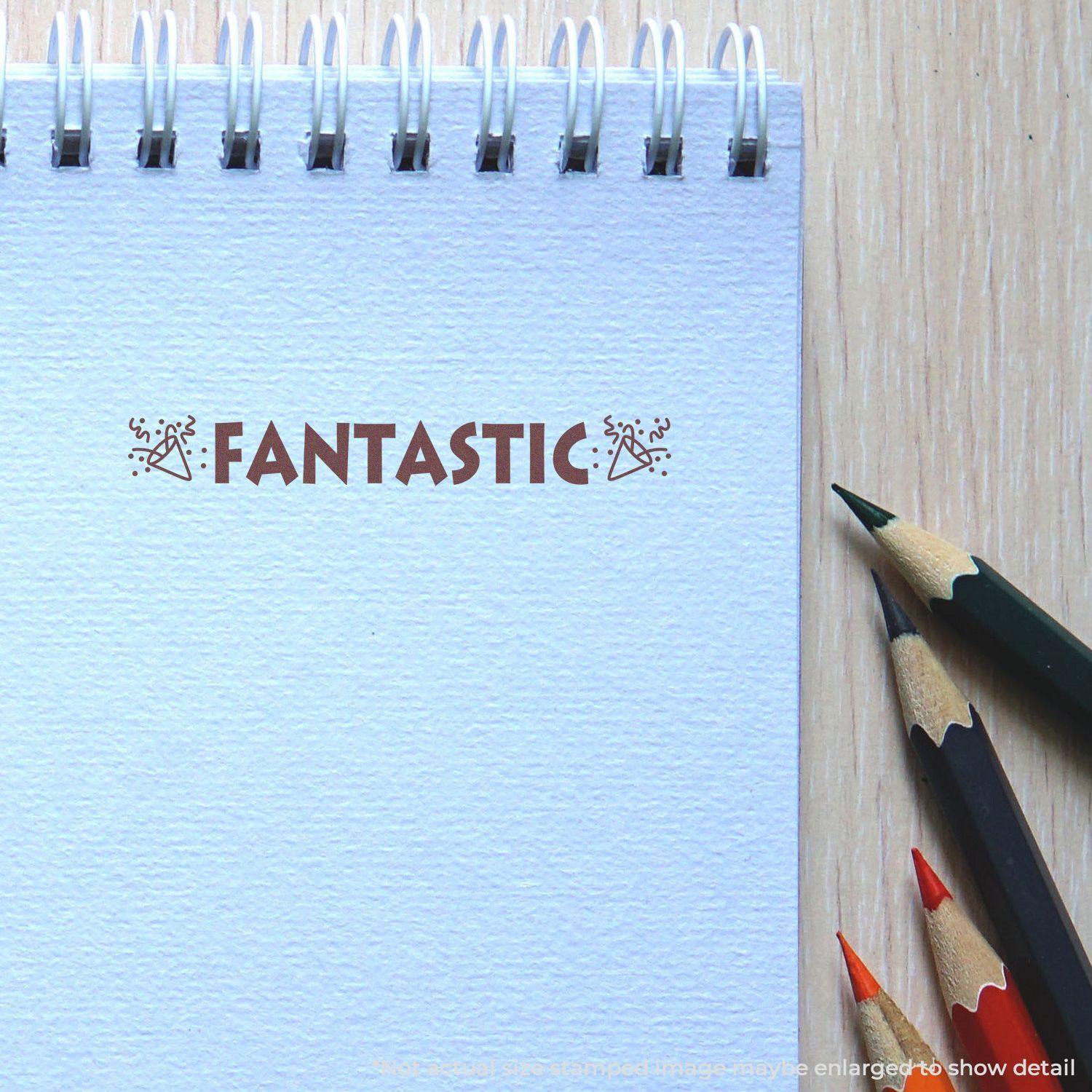 A Fantastic with Icons Rubber Stamp imprint on a spiral notebook, surrounded by colored pencils on a wooden surface.