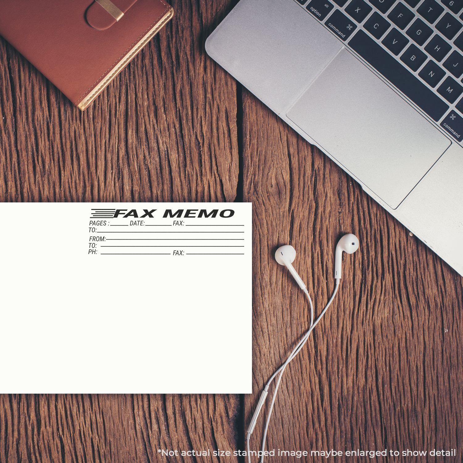 Slim Pre-Inked Fax Memo Stamp used on a fax memo sheet placed on a wooden desk beside a laptop, notebook, and earphones.