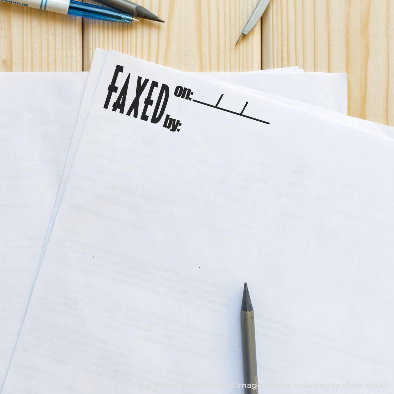 Large Pre-Inked Faxed on Stamp marking a document on a wooden desk with pens and papers scattered around.