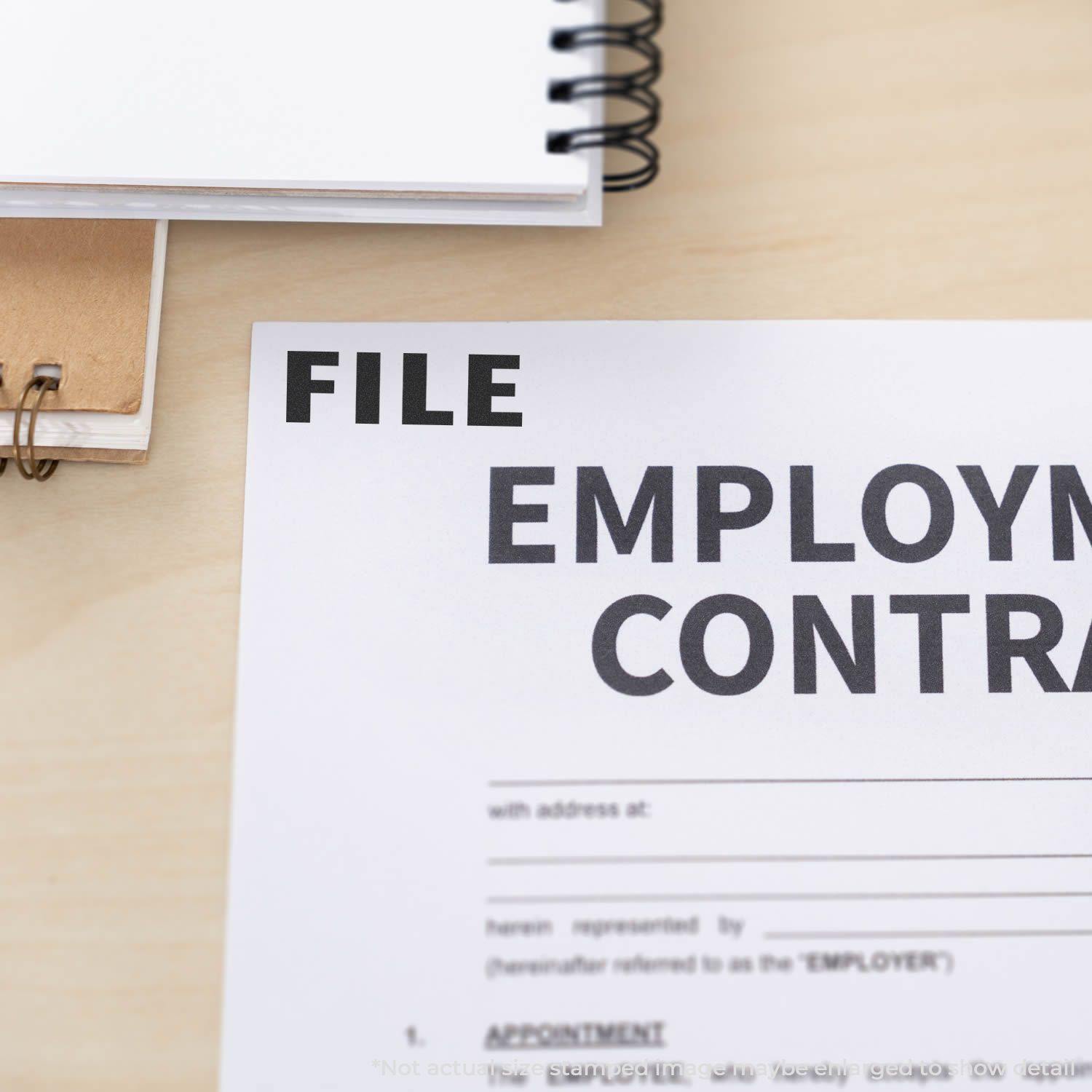 Large File Rubber Stamp marking 'FILE' on an employment contract, with notebooks in the background on a wooden desk.