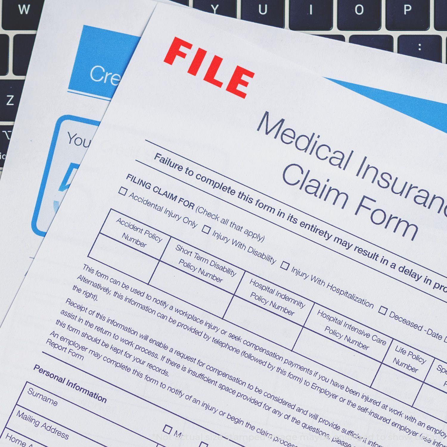 Medical insurance claim forms stamped with a red FILE Rubber Stamp, placed on a laptop keyboard.