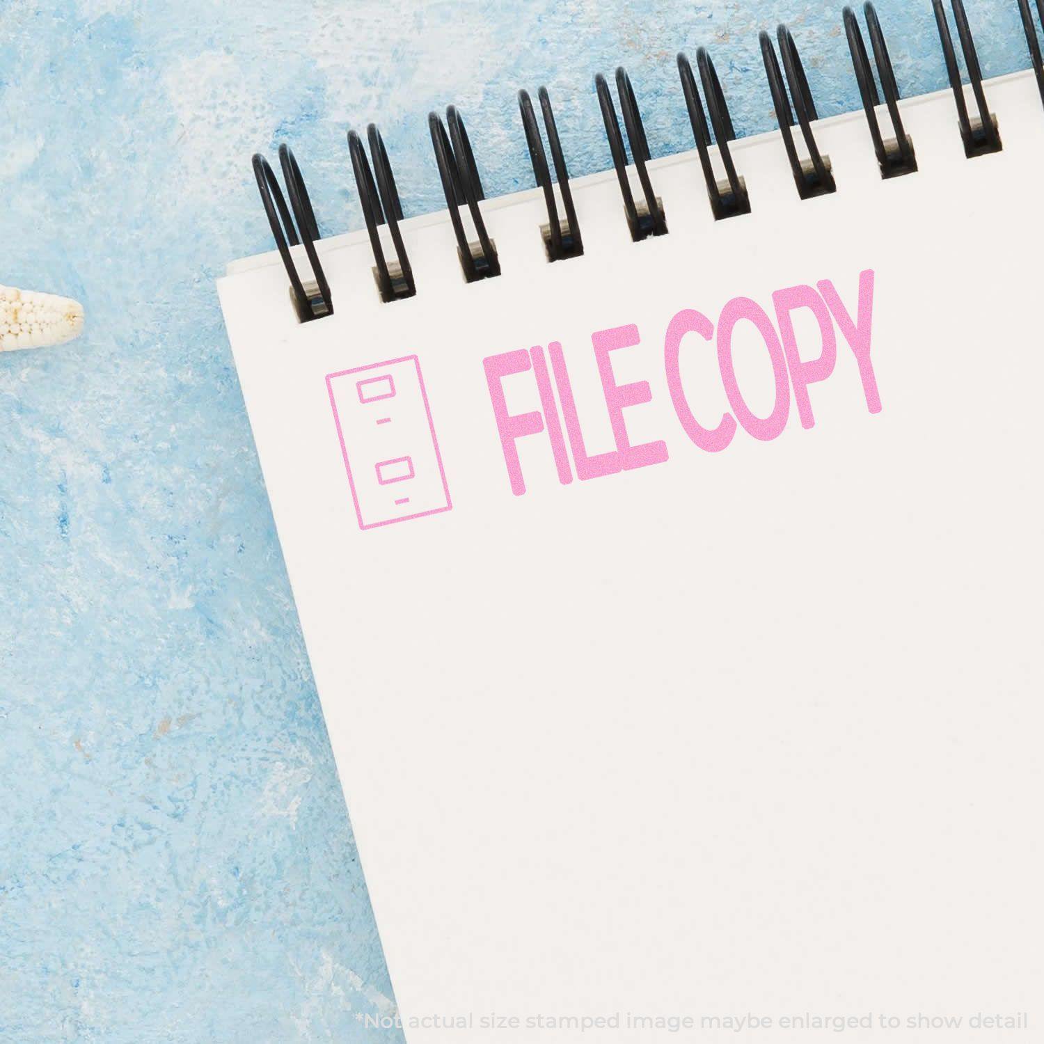 Large Pre-Inked File Copy with Drawer Stamp in pink ink on a spiral notebook, placed on a light blue textured surface.