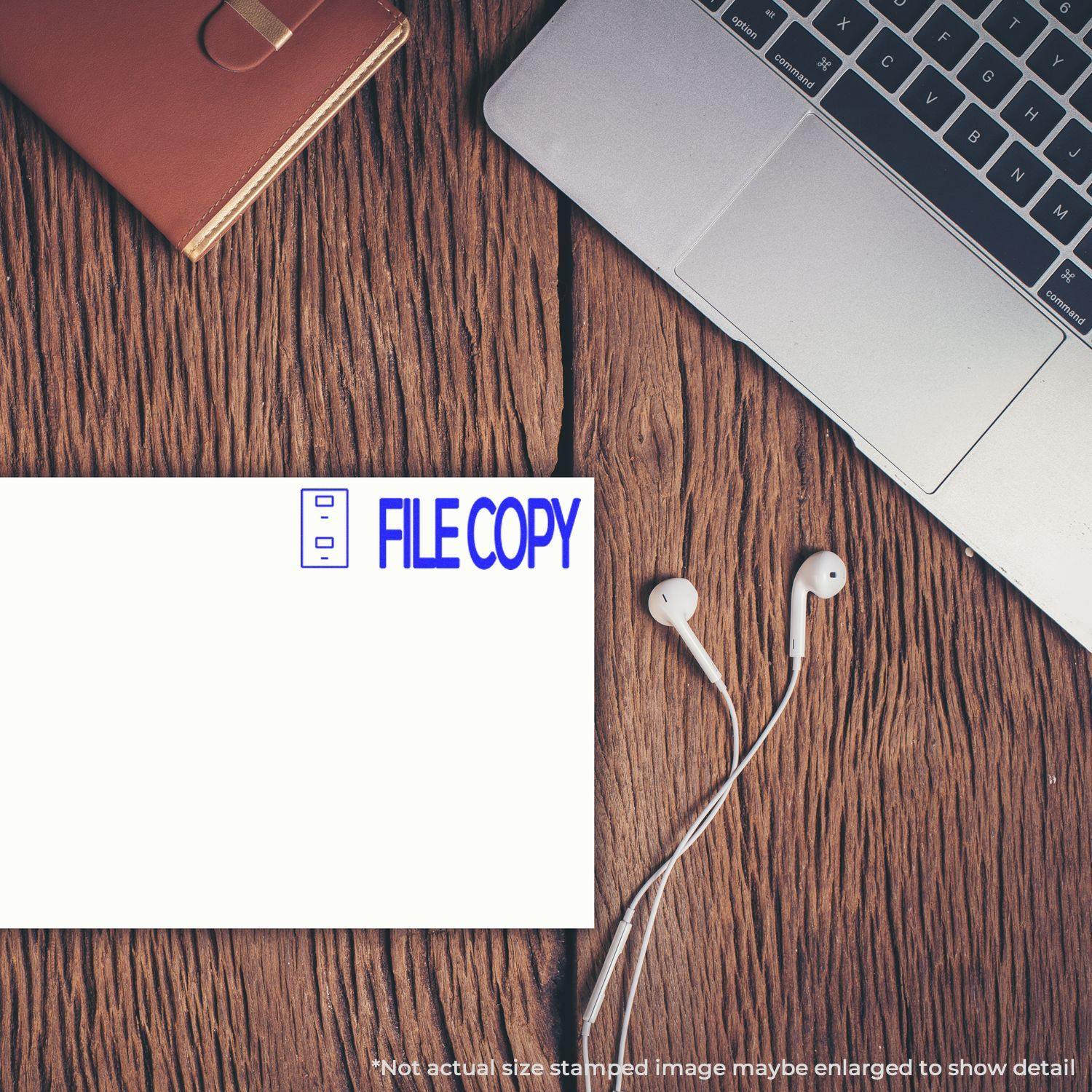 File Copy with Drawer Rubber Stamp used on a document placed on a wooden desk beside a laptop, earphones, and a notebook.