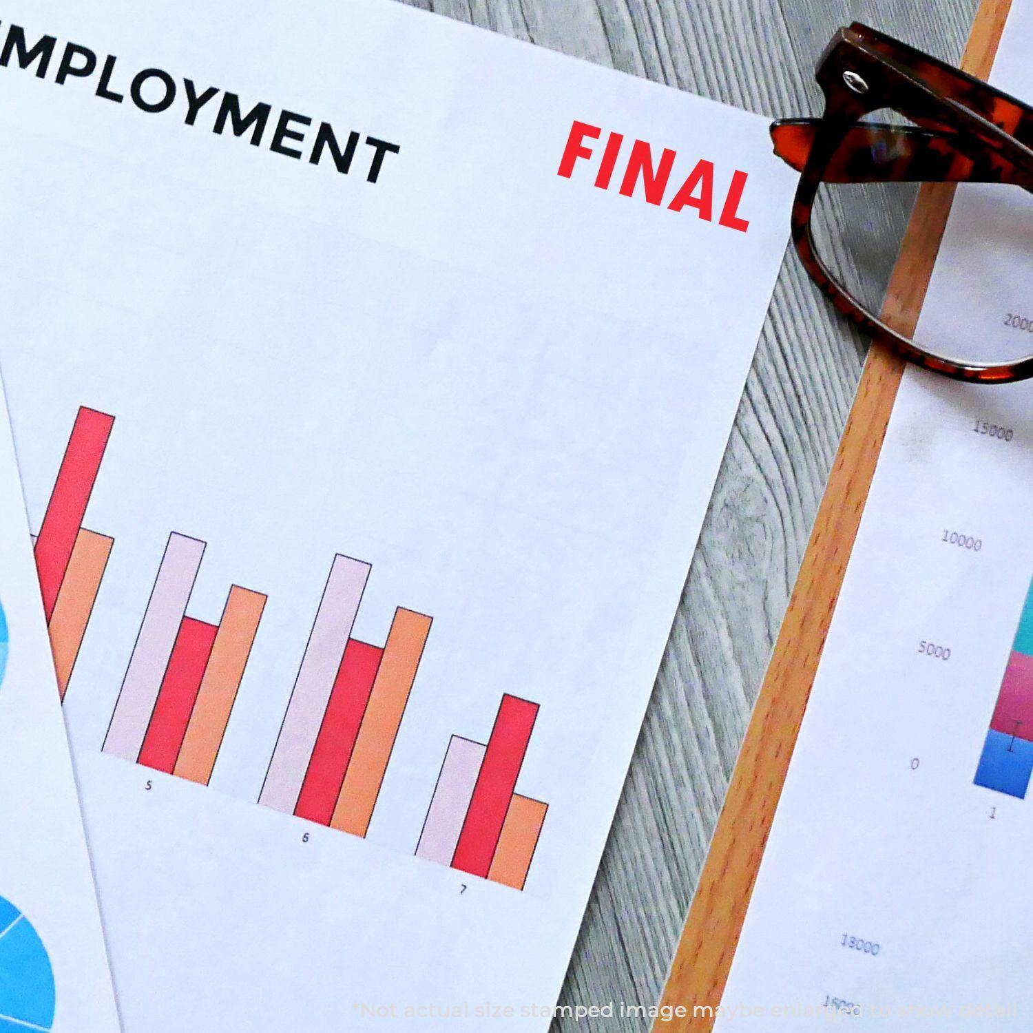 A document stamped with FINAL using a Slim Pre-Inked Final Stamp, next to a chart and a pair of glasses on a desk.