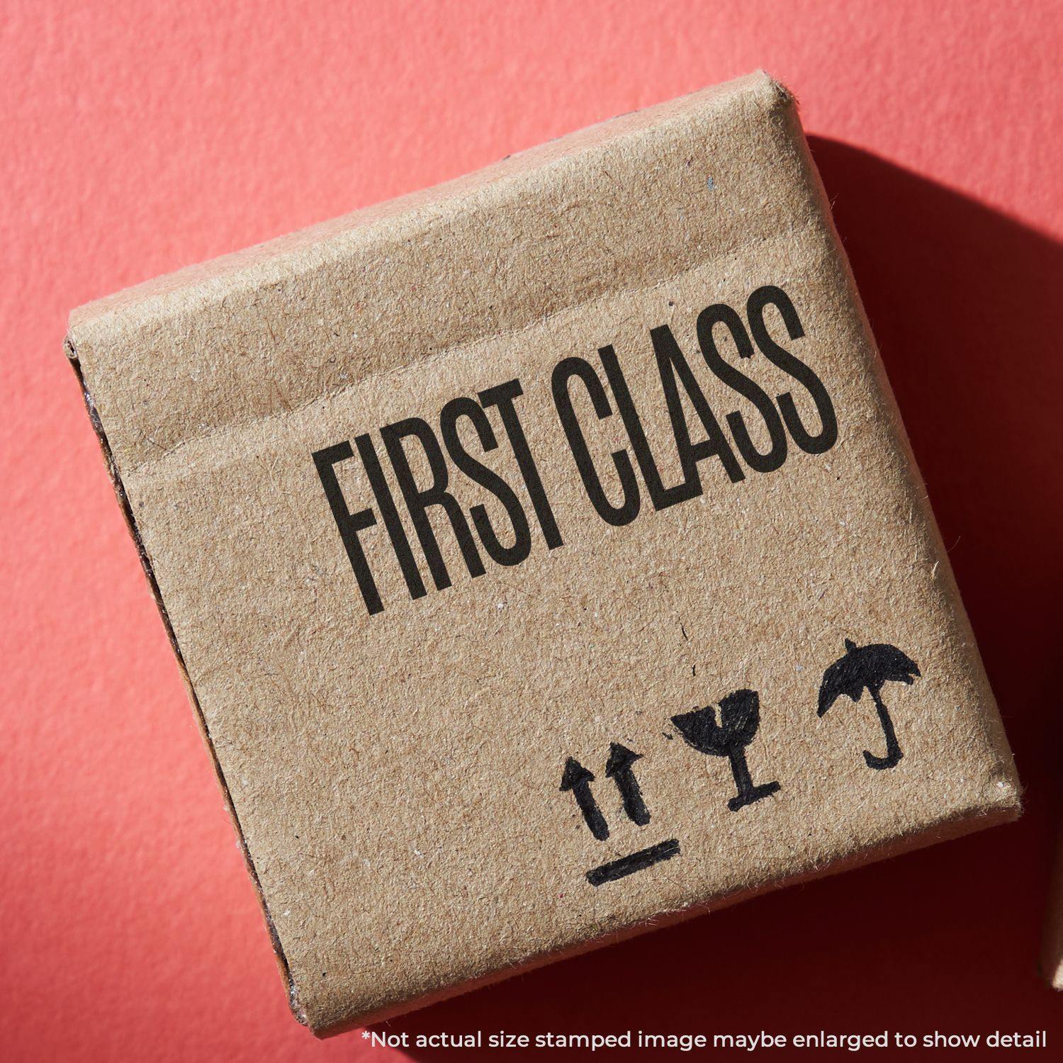 Large First Class Rubber Stamp used on a brown cardboard box with FIRST CLASS text and shipping symbols on a red background.