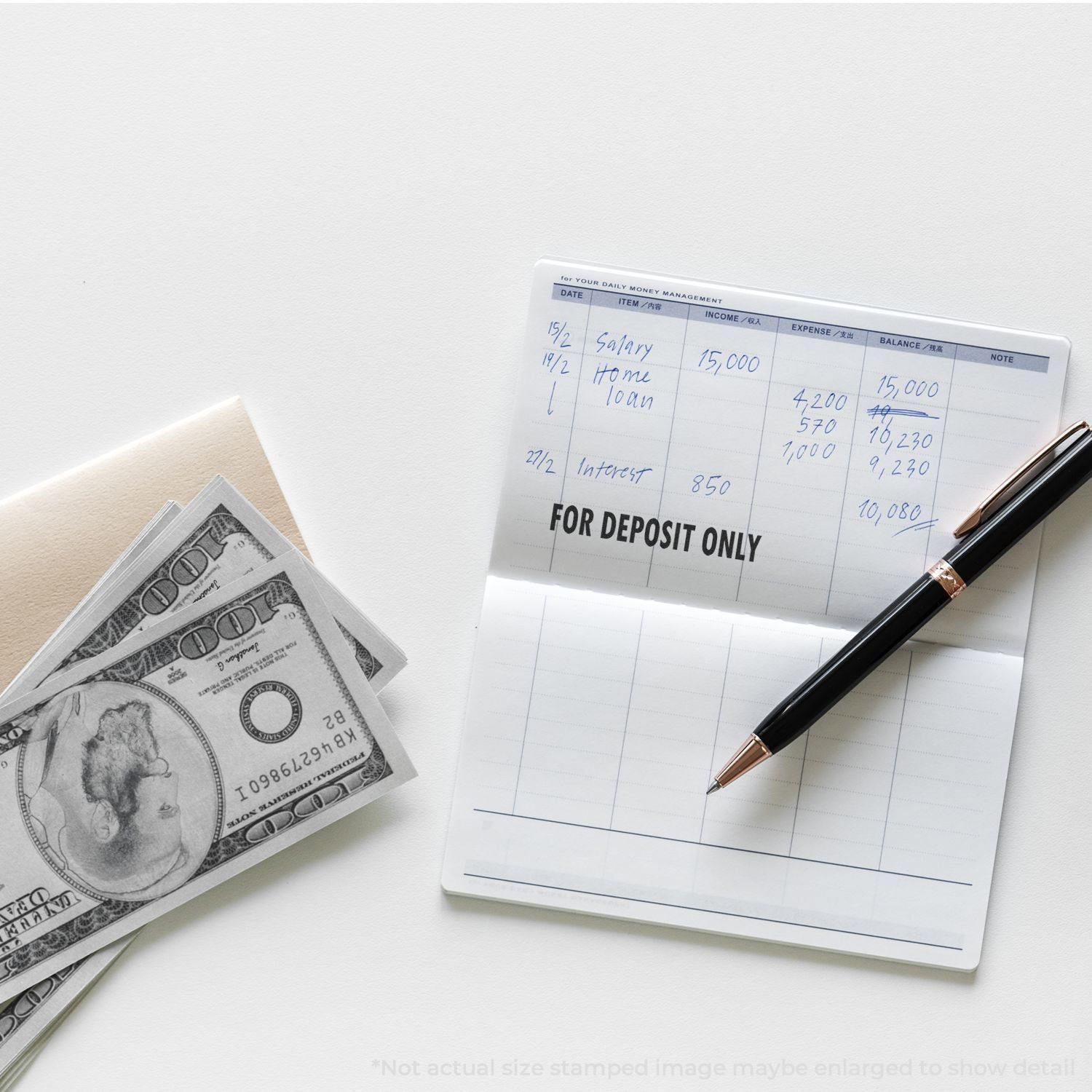 A checkbook with a For Deposit Only Rubber Stamp imprint, a pen, and a stack of hundred-dollar bills on a white surface.