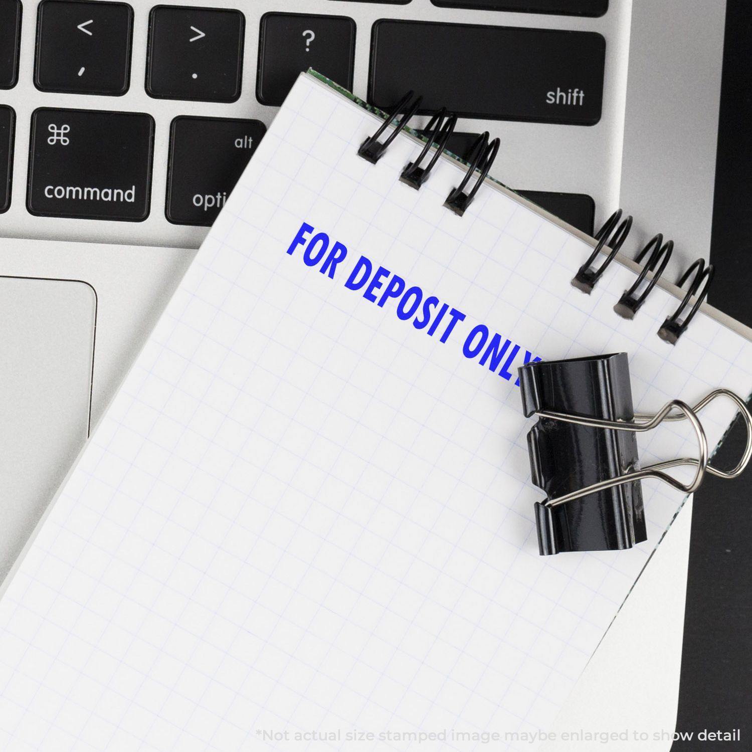 A For Deposit Only Rubber Stamp imprint on a notepad, placed on a laptop keyboard with a black binder clip attached.