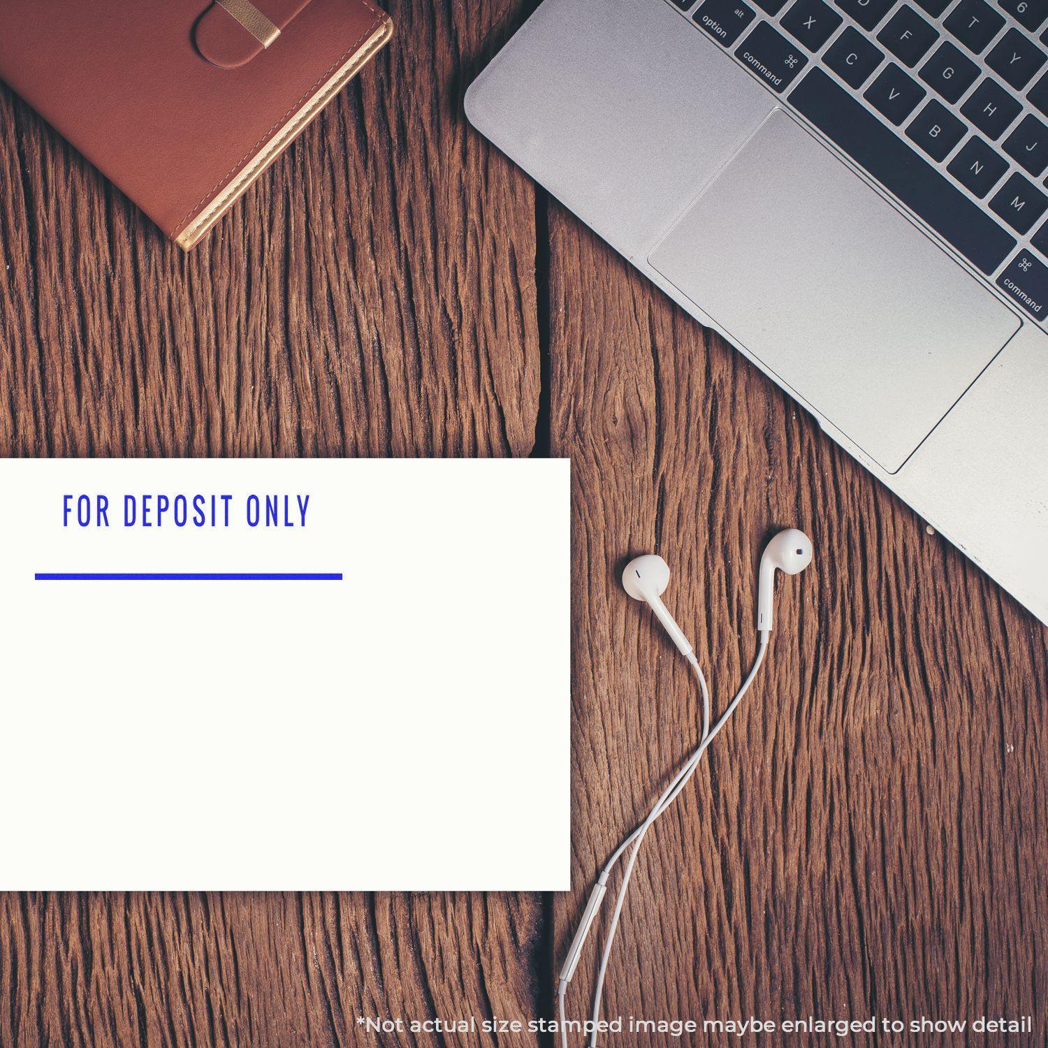 A Large Self Inking For Deposit Only with Line Stamp is shown on a wooden desk beside a laptop, notebook, and earphones.