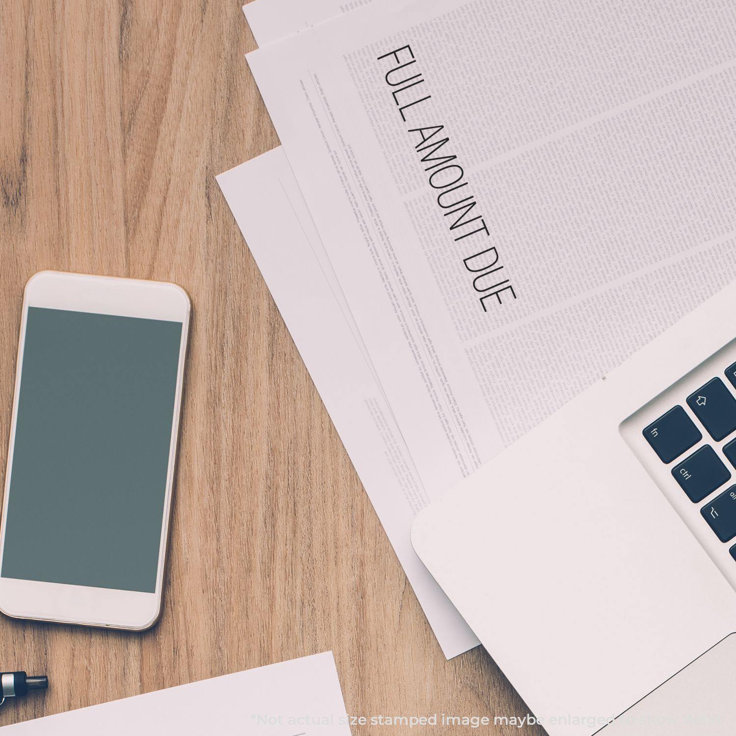 A desk with a phone, laptop, and documents stamped FULL AMOUNT DUE using the Large Full Amount Due Rubber Stamp.