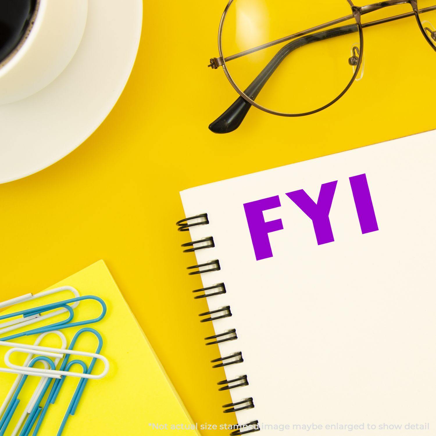 A notebook stamped with FYI using the FYI Rubber Stamp, placed on a yellow desk with a cup, glasses, and paper clips.