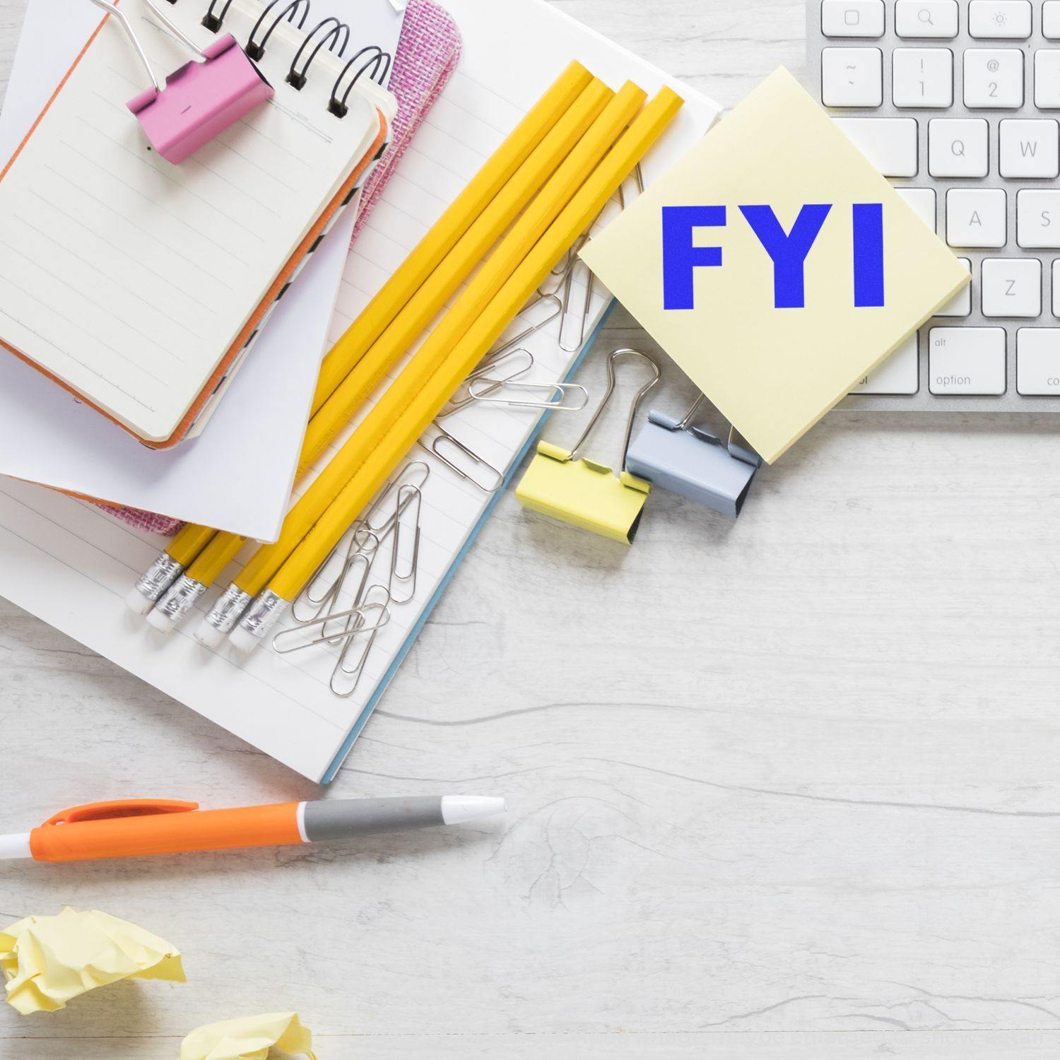 Desk with notepad, pencils, paper clips, and a sticky note stamped with FYI using the FYI Rubber Stamp, next to a keyboard.