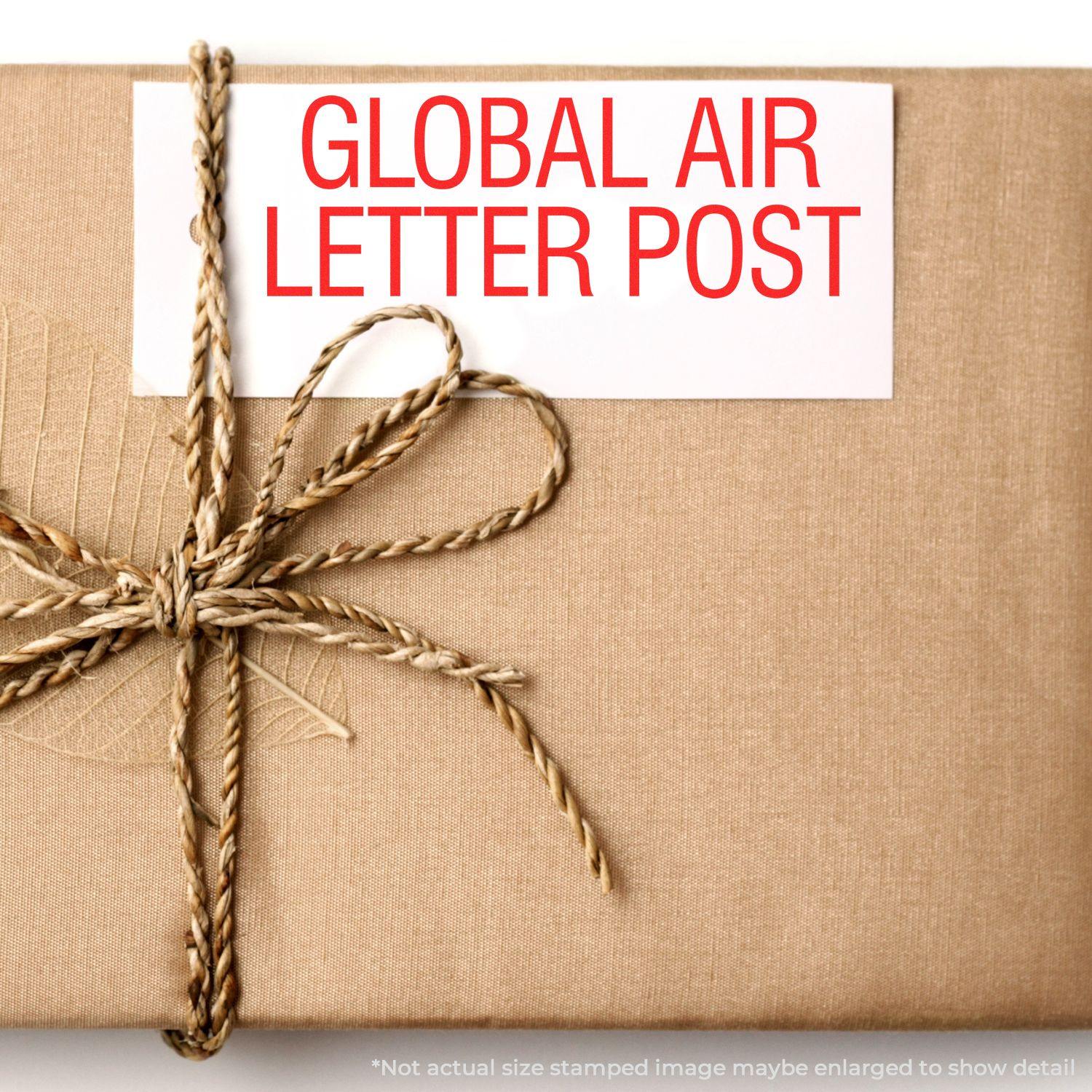 A package wrapped in brown paper with twine, featuring a Self Inking Global Air Letter Post Stamp in red text on a white label.