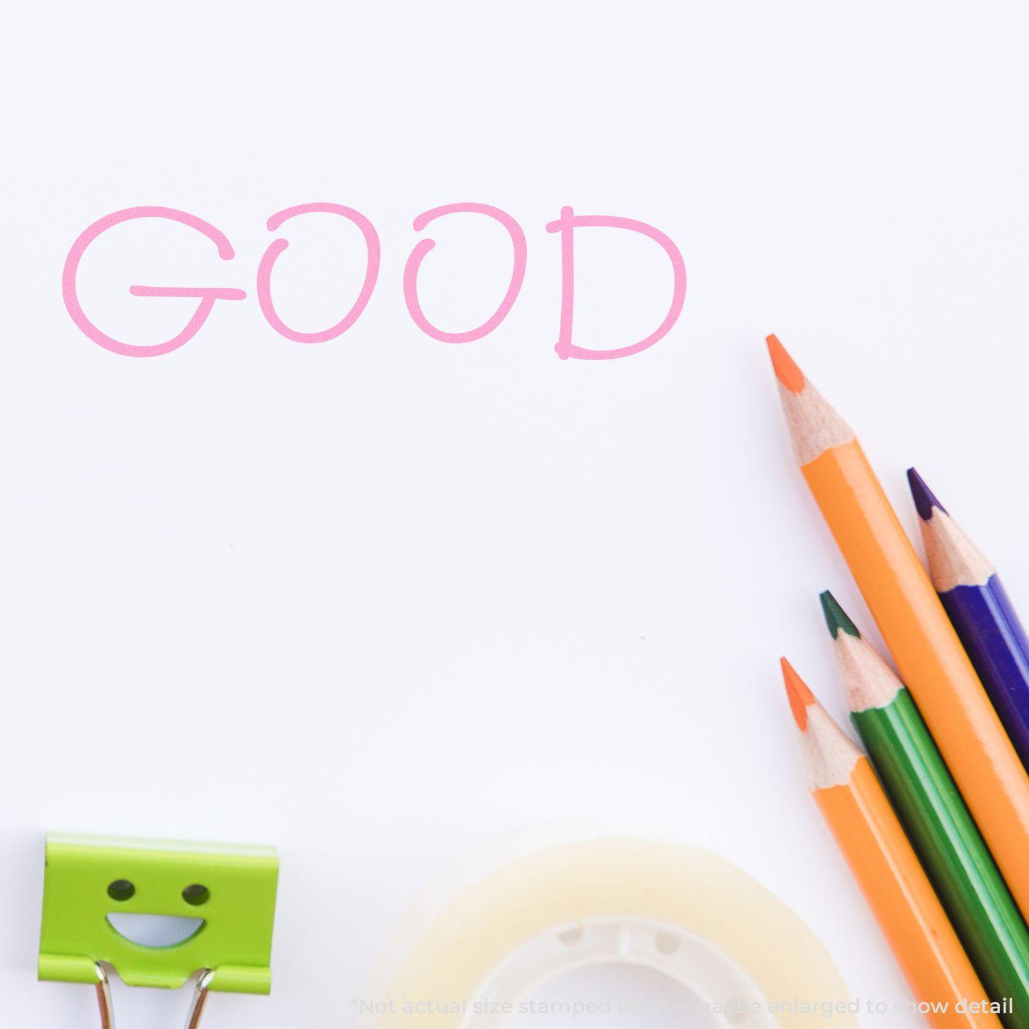 Large Good Rubber Stamp imprint on white paper with colorful pencils, a smiling binder clip, and tape in the background.