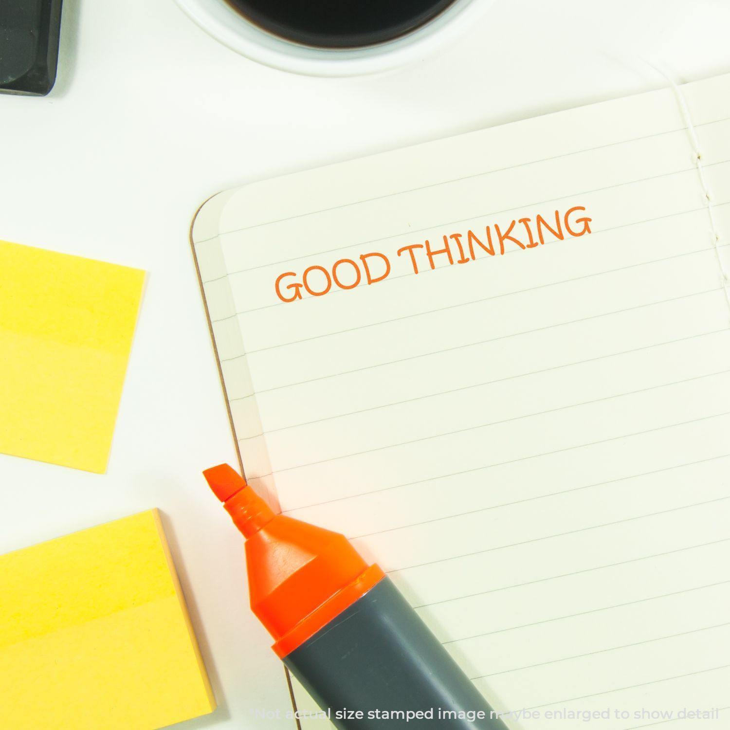 Large Good Thinking Rubber Stamp used on a notebook, with a highlighter and sticky notes nearby on a white desk.