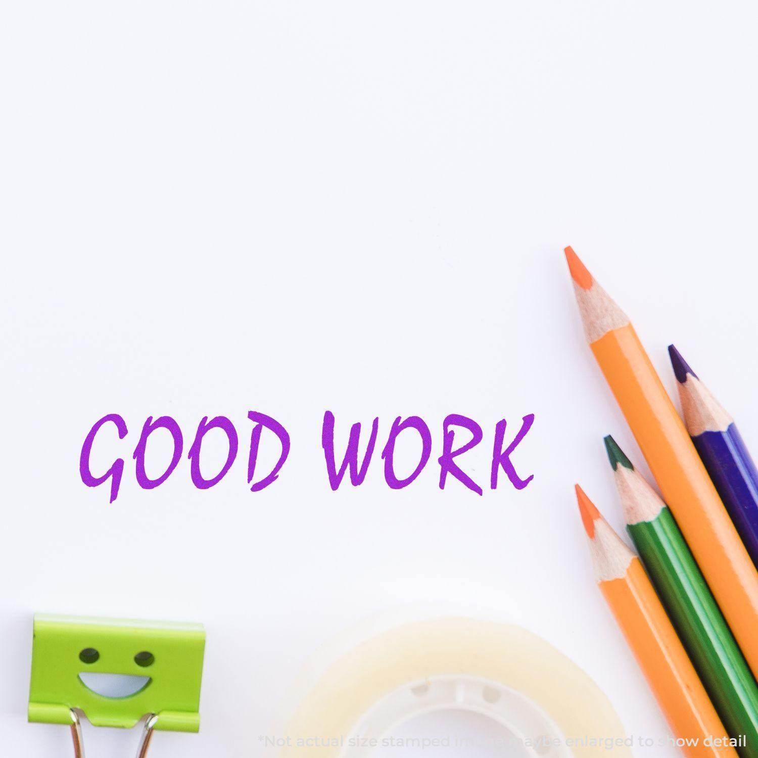 Good Work Rubber Stamp impression in purple ink on white paper, surrounded by colorful pencils, a smiley face clip, and tape.