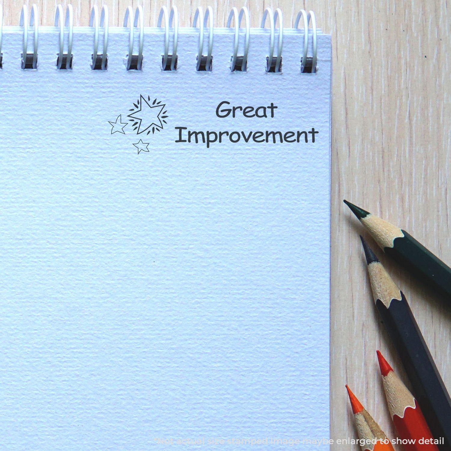 A notebook with a Great Improvement mark from the Large Pre-Inked Great Improvement Stamp, next to colored pencils on a wooden surface.