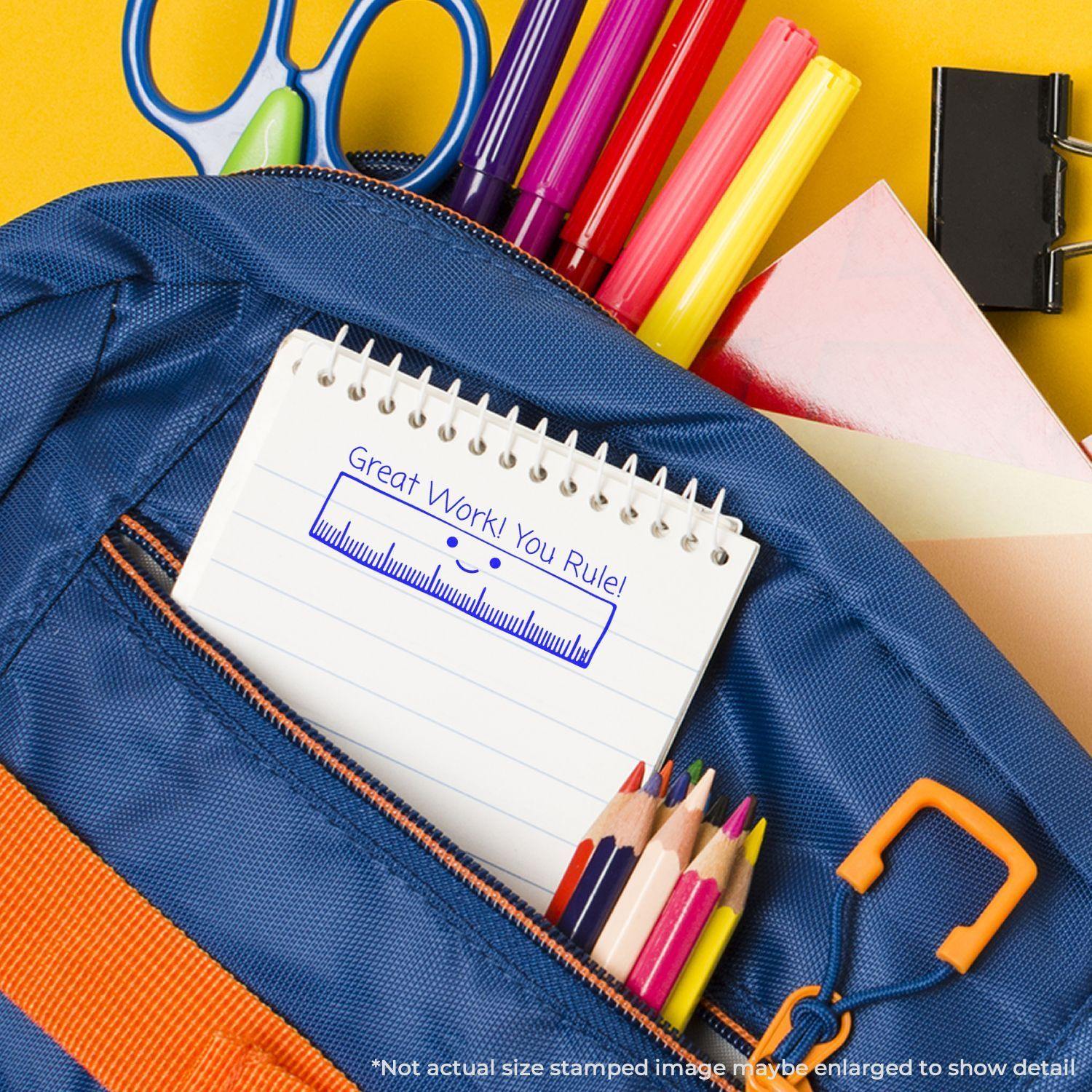 A blue backpack with colored pencils, pens, and a notebook stamped with Great Work! You Rule! using the Great Work You Rule Rubber Stamp.