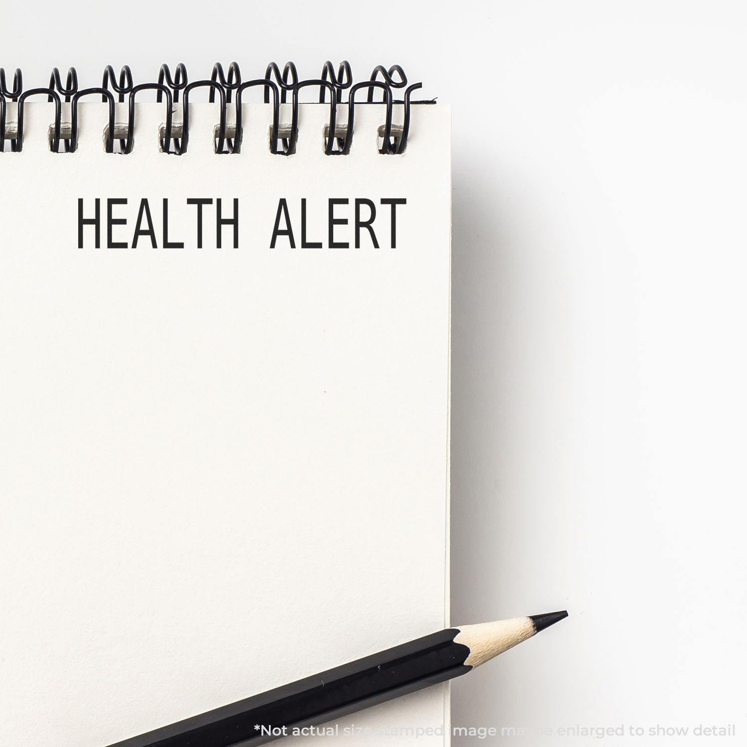 Notebook stamped with 'HEALTH ALERT' using Slim Pre-Inked Health Alert Stamp, with a pencil placed beside it on a white background.