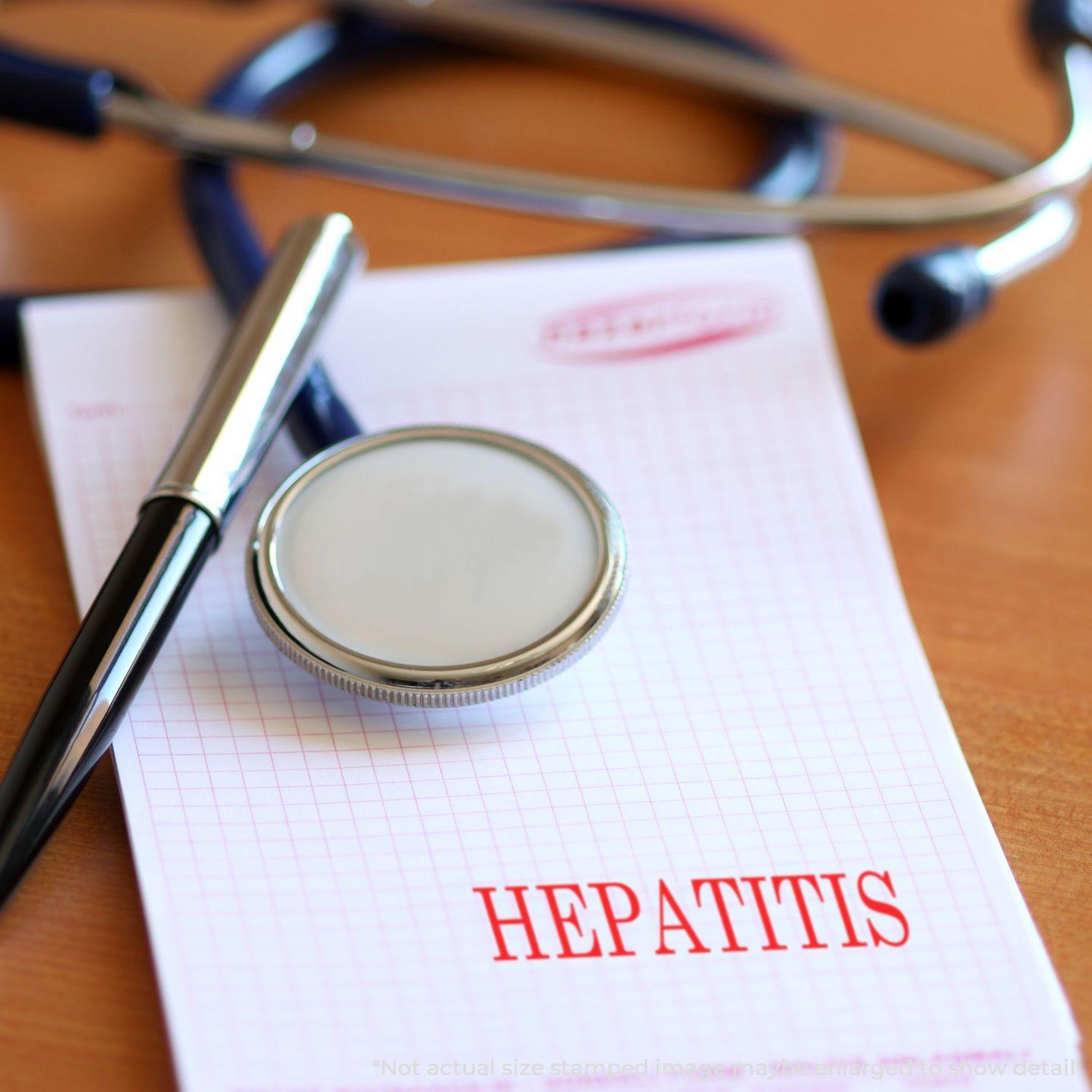 A stethoscope, pen, and Large Pre-Inked Hepatitis Stamp on a notepad with HEPATITIS stamped in red.