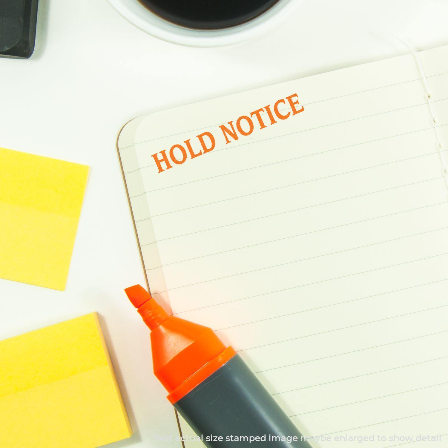 Hold Notice Rubber Stamp used on a lined notebook, with a highlighter, sticky notes, and a coffee cup nearby.