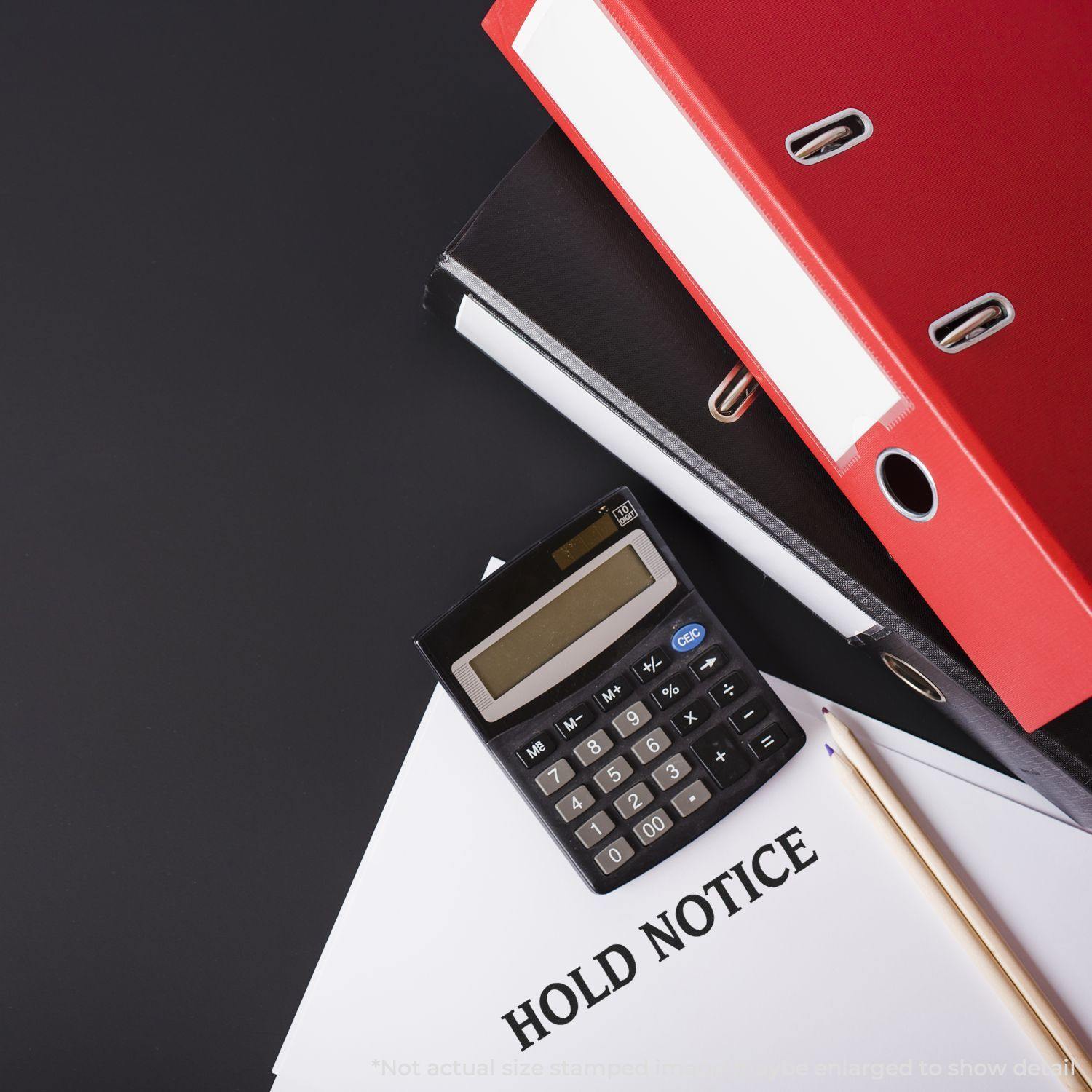 Large Pre-Inked Hold Notice Stamp used on a document, with a calculator, pencil, and red binders in the background.