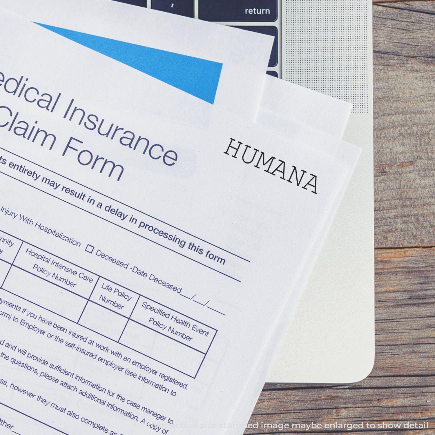 Medical insurance claim forms stamped with HUMANA using the Humana Rubber Stamp, placed on a laptop keyboard.