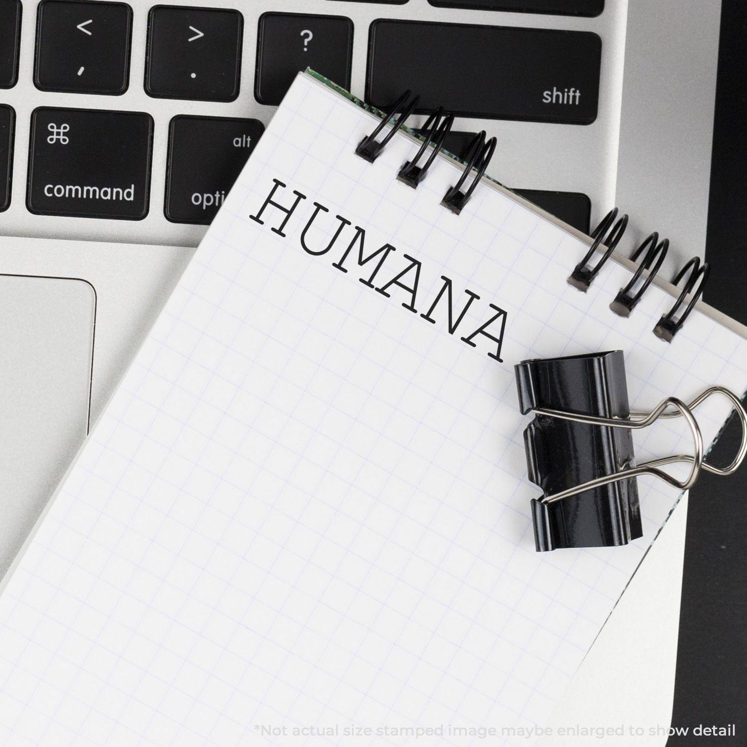 A Humana Rubber Stamp imprint on a notepad with a binder clip, placed on a laptop keyboard.