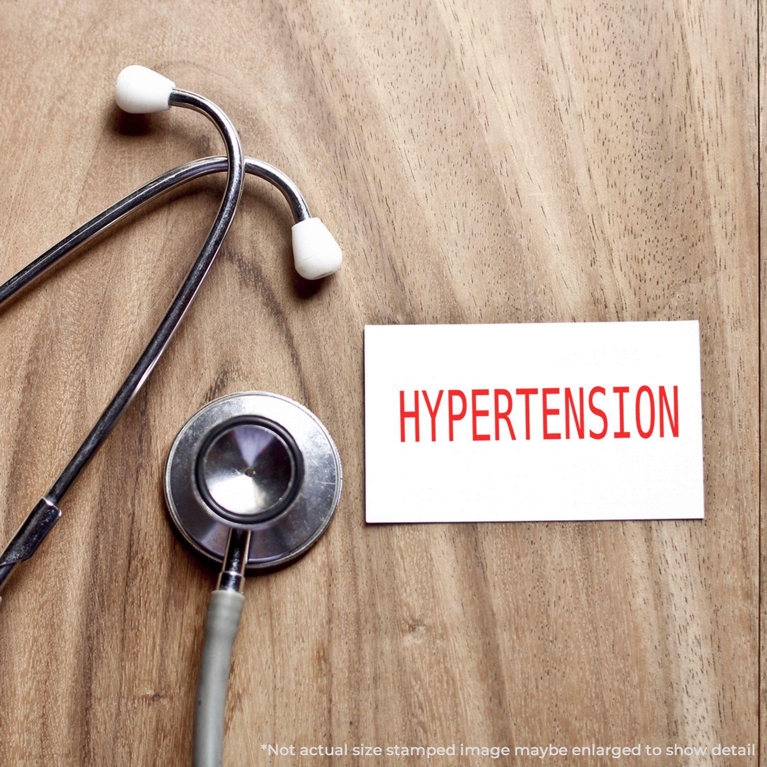 A stethoscope next to a card stamped with HYPERTENSION using the Large Pre-Inked Hypertension Stamp on a wooden surface.