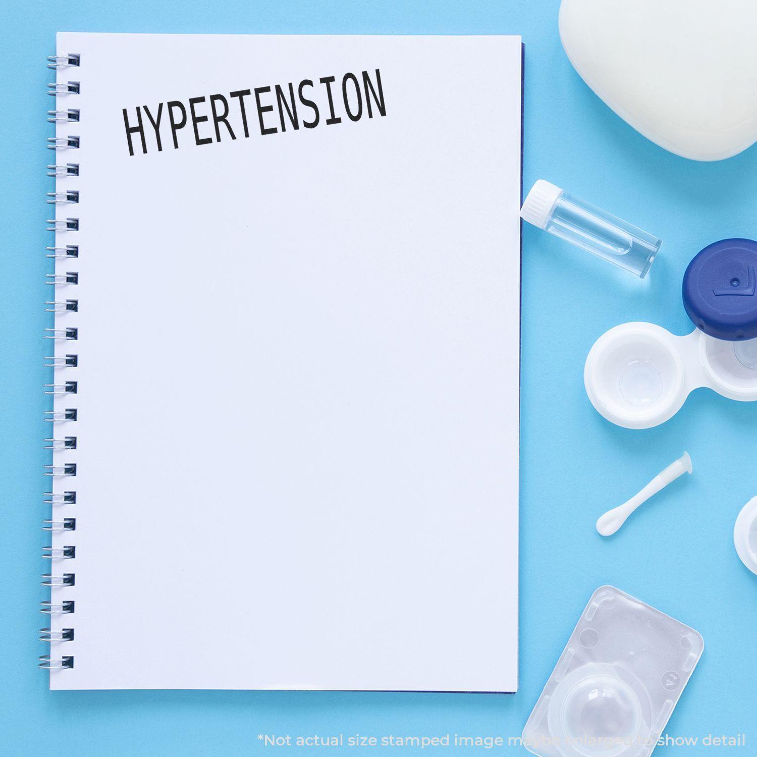 Hypertension Rubber Stamp on a white spiral notebook, surrounded by medical items on a blue background.