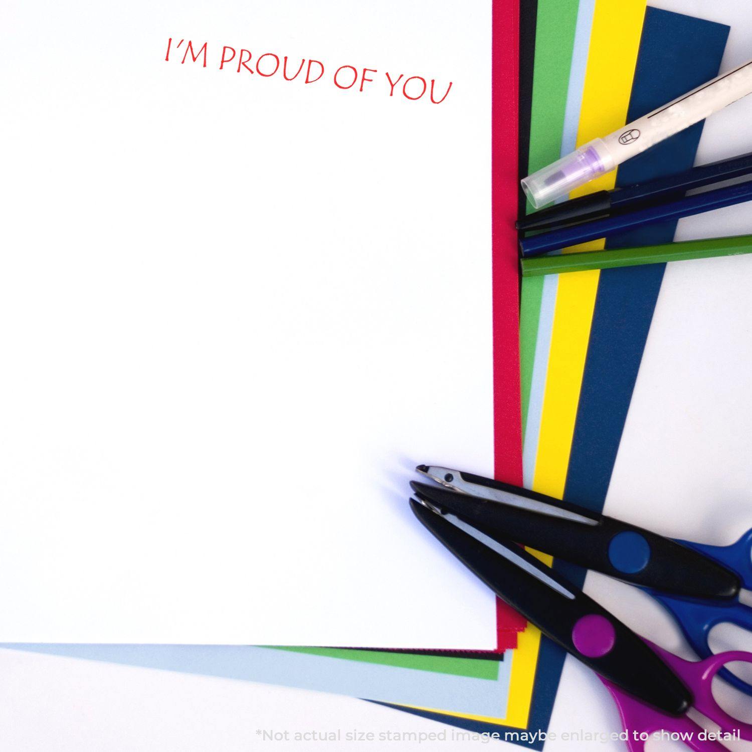 Large Self Inking I'm Proud Of You Stamp used on white paper, surrounded by colorful sheets, scissors, and pens.