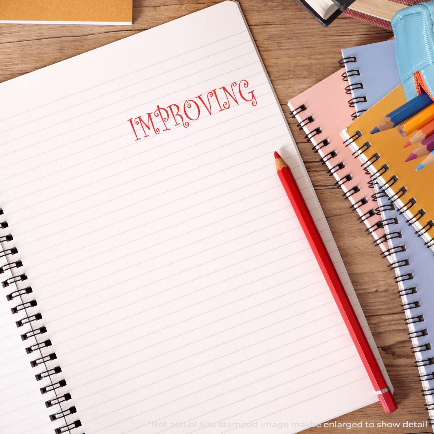 Notebook with the word 'IMPROVING' stamped in red using the Improving Rubber Stamp, surrounded by stationery items on a wooden desk.