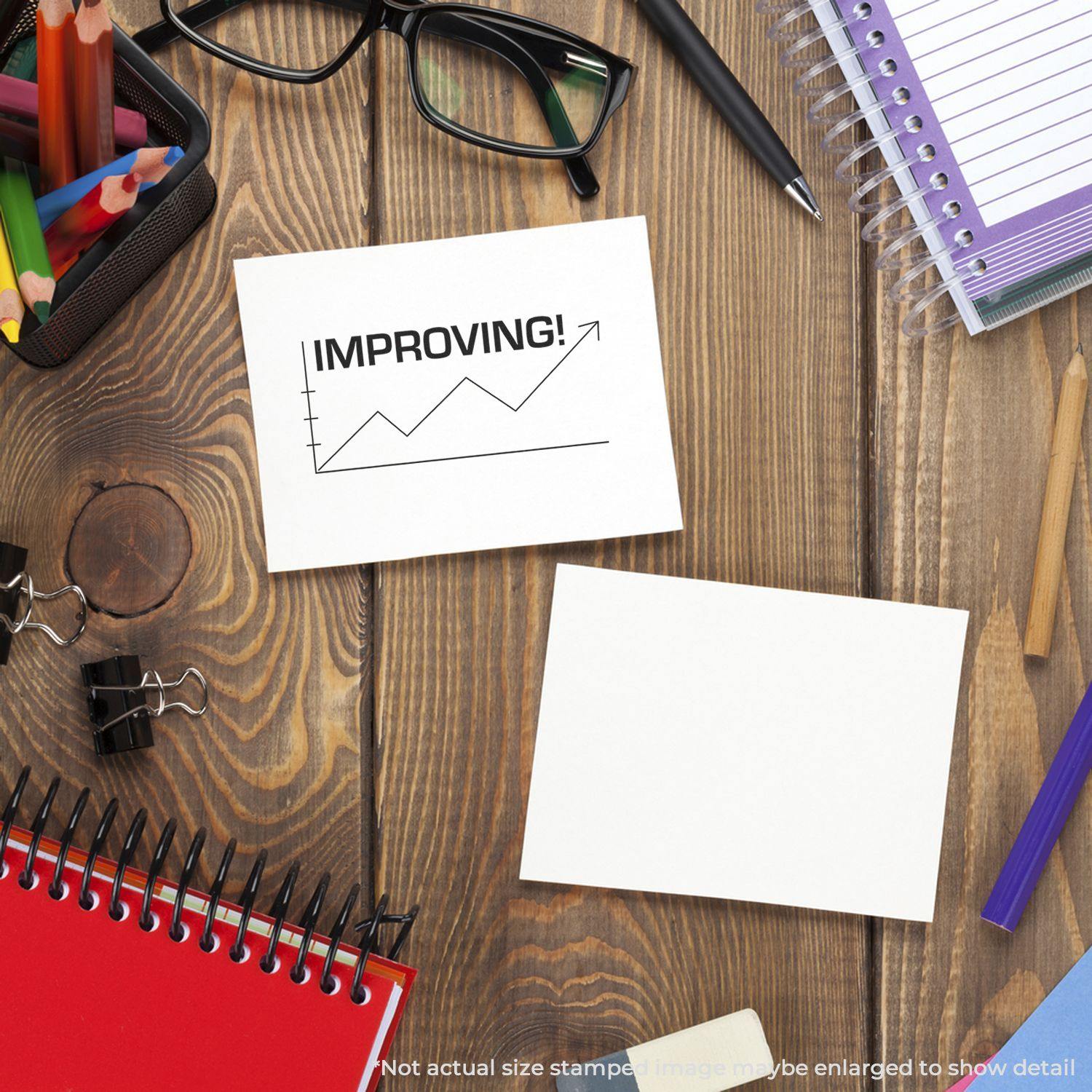 Large Self Inking Improving with Chart Icon Stamp on a desk with stationery, showing a card stamped with an upward trend chart and IMPROVING!