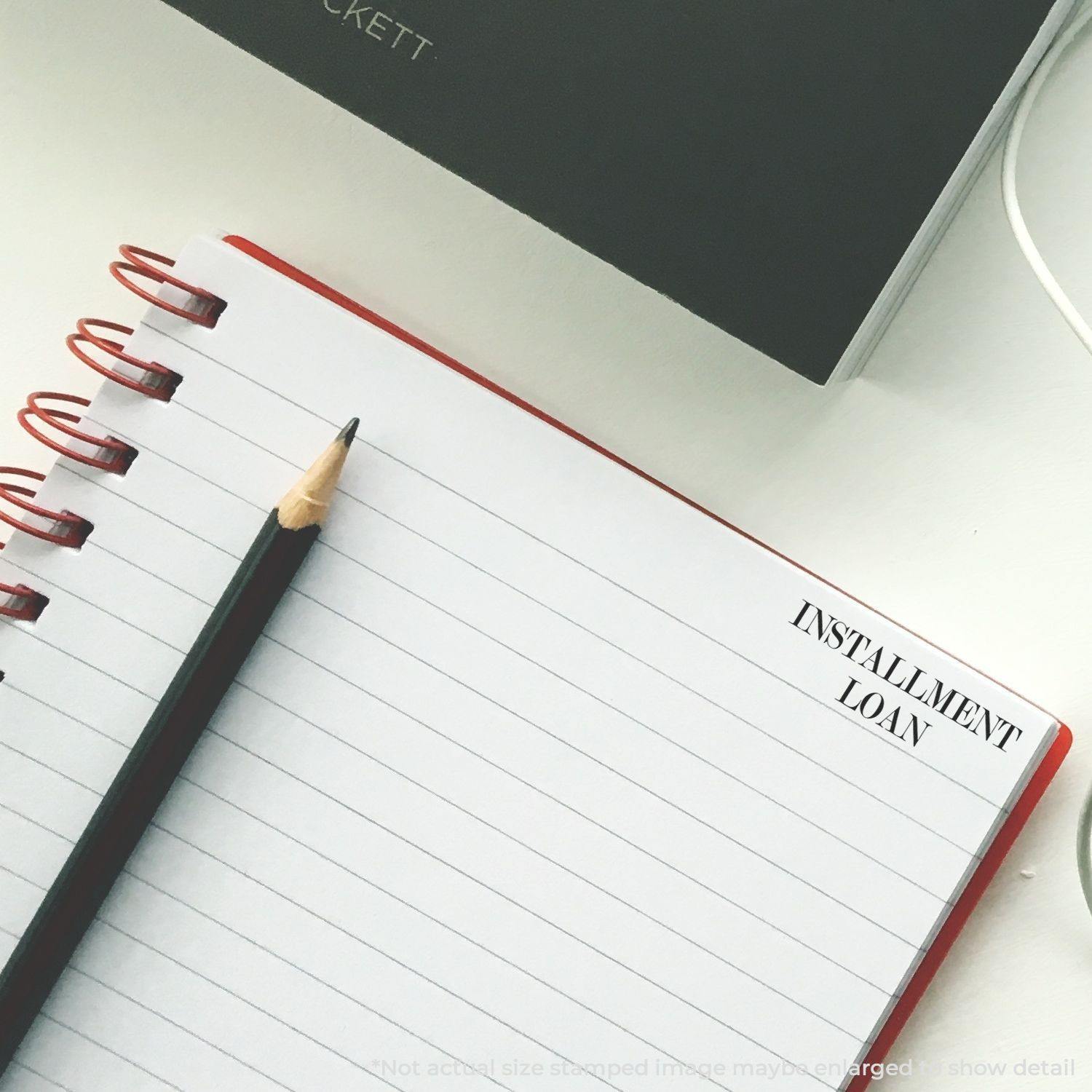 A notebook with a pencil and an Installment Loan rubber stamp impression on the top right corner of the page.