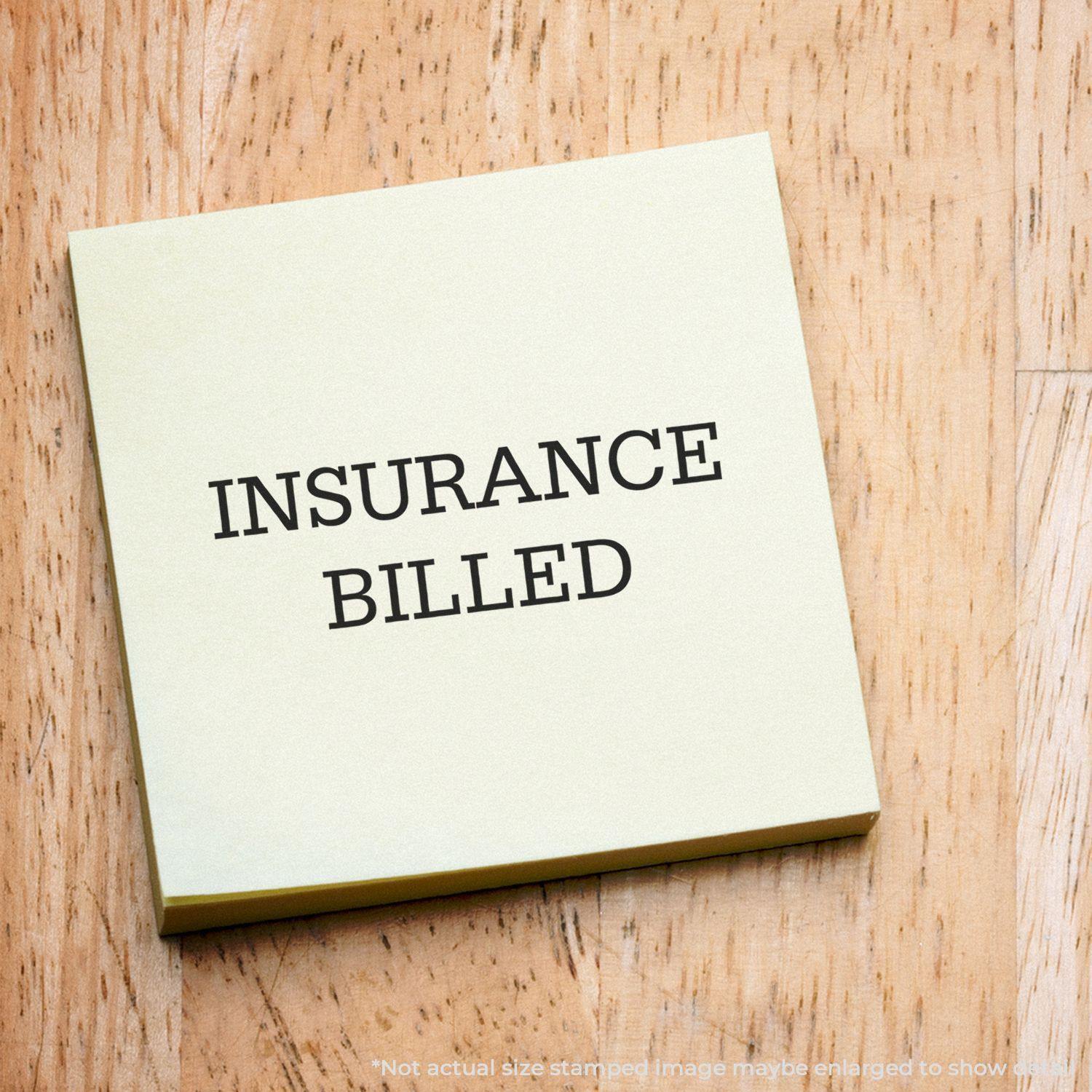 Large Self Inking Insurance Billed Stamp used on a yellow sticky note placed on a wooden surface.