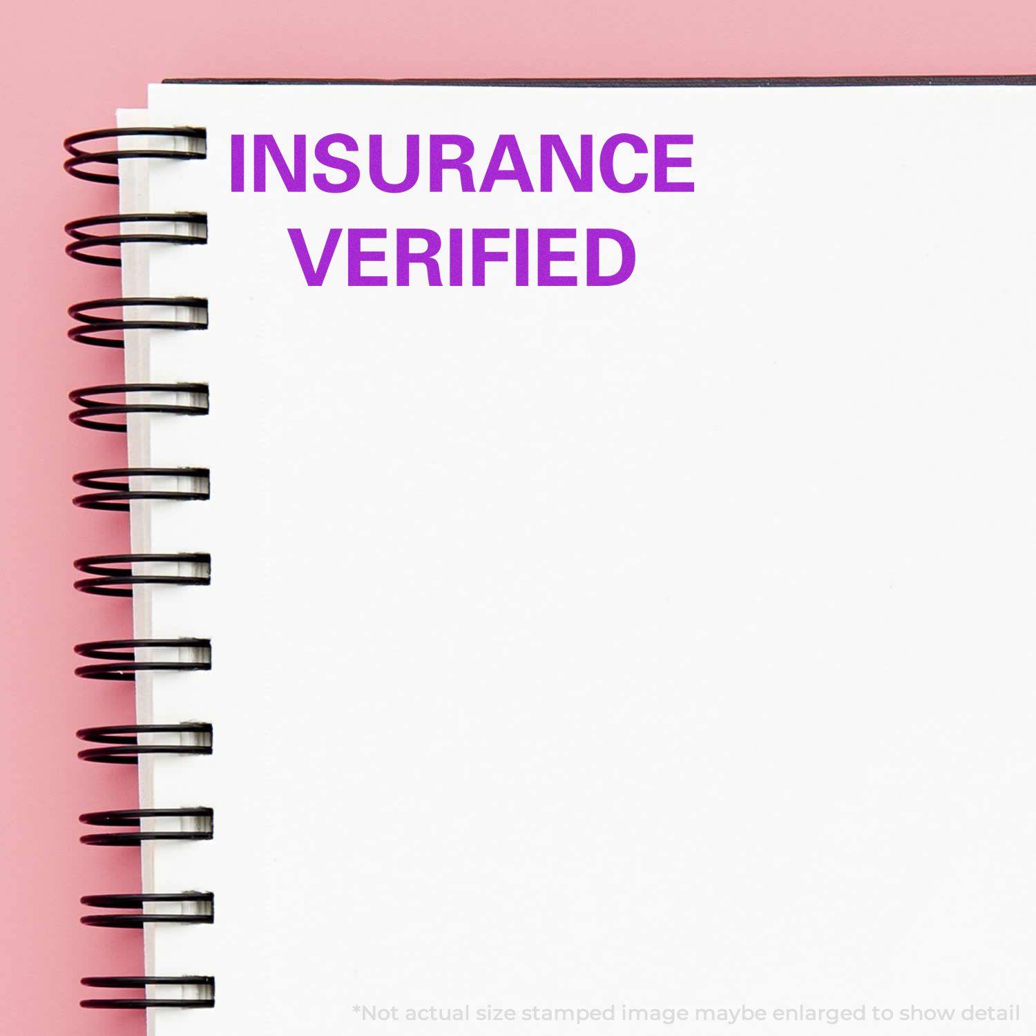 Large Insurance Verified Rubber Stamp imprint on a white spiral notebook with a pink background.