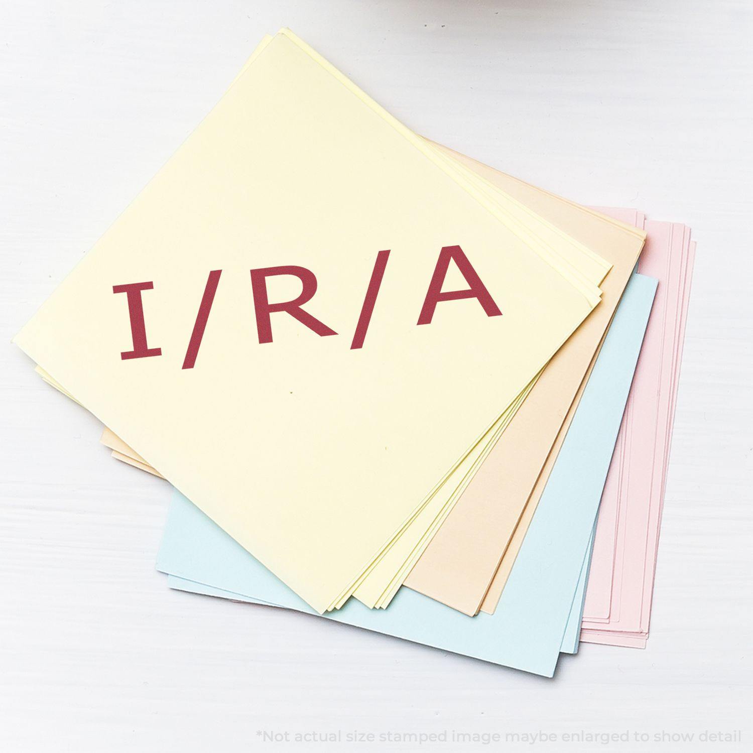 Large I/R/A Rubber Stamp used on a stack of pastel-colored papers, displaying the stamped letters I/R/A in bold red ink.