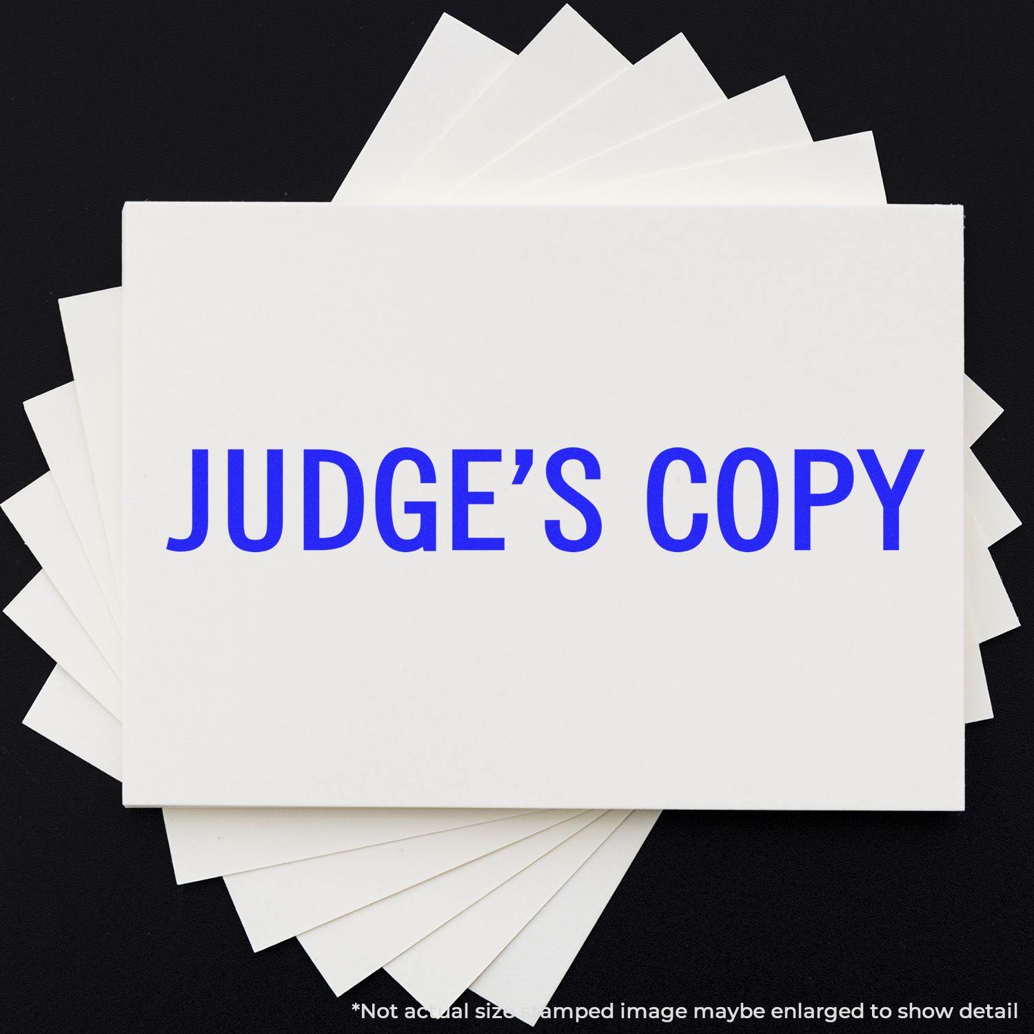 Large Pre-Inked Judge's Copy Stamp in blue ink on a white paper stack, displayed on a black background.