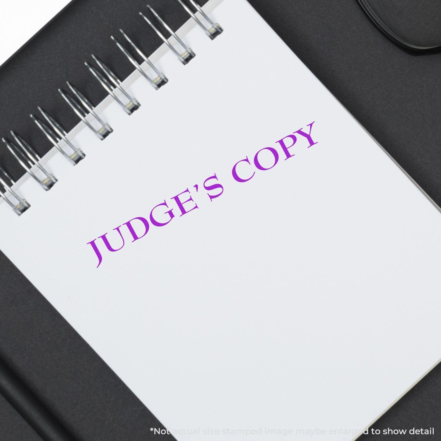 Slim Pre-Inked Judges Copy Stamp in purple ink on a white spiral notebook, placed on a black surface.