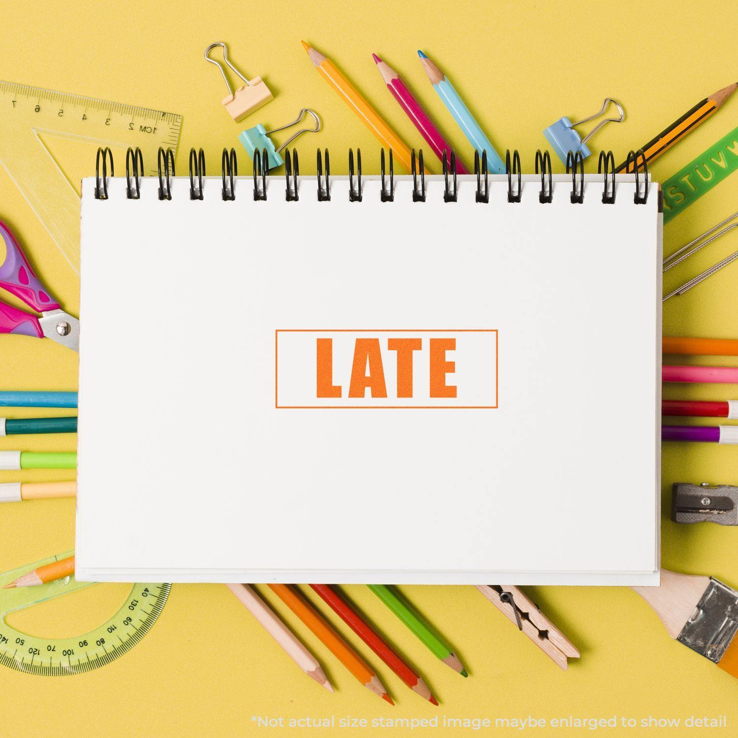 Large Pre-Inked Late with Border Stamp in use on a white notebook, surrounded by colorful stationery on a yellow background.