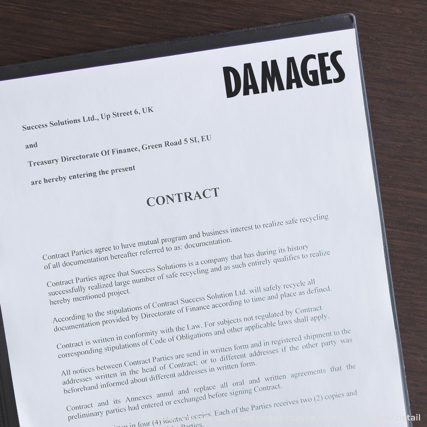 Large Pre-Inked Damages Stamp marking the word DAMAGES on a legal contract document placed on a wooden surface.