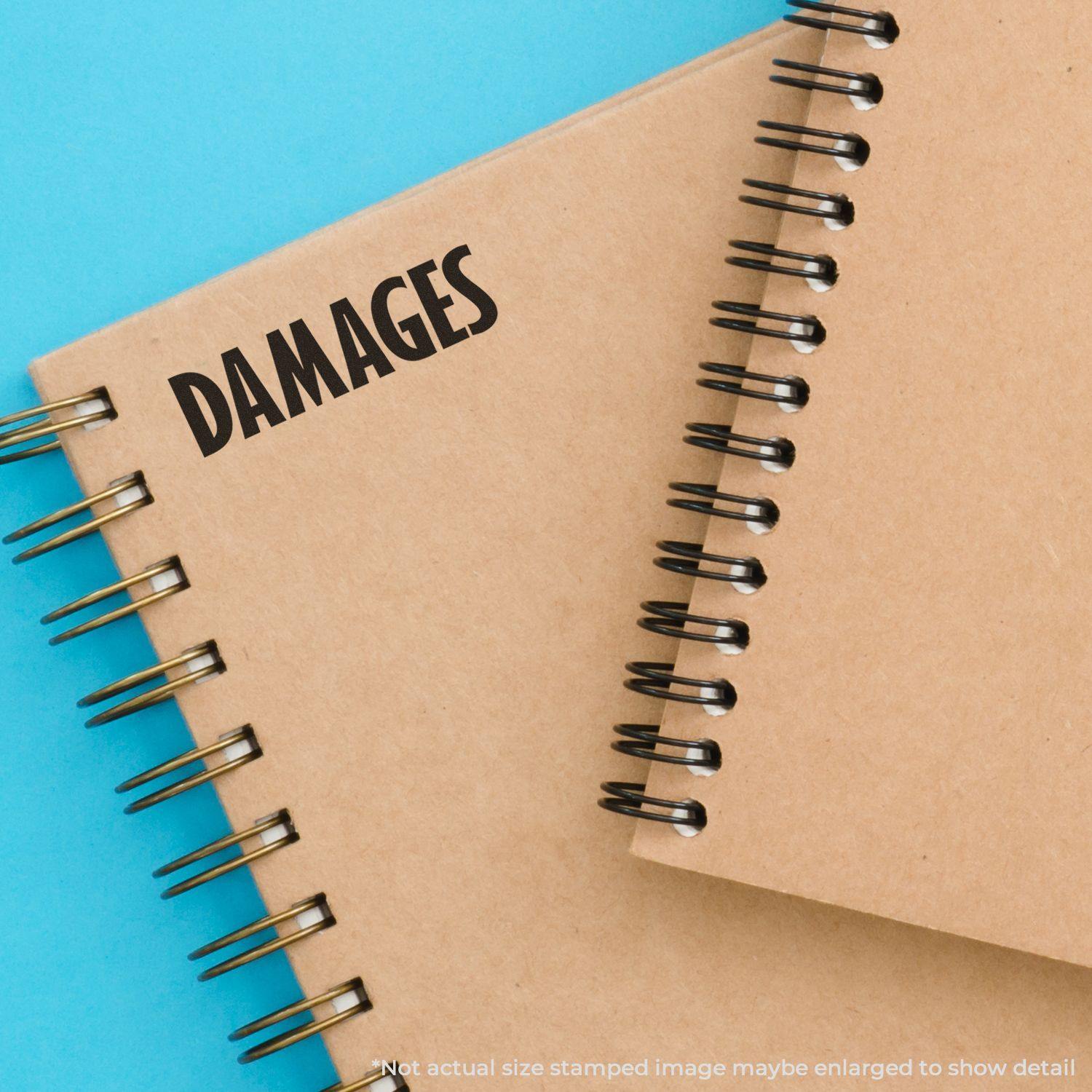 Large Damages Rubber Stamp used on a brown spiral notebook with a blue background. Text reads DAMAGES in bold black letters.