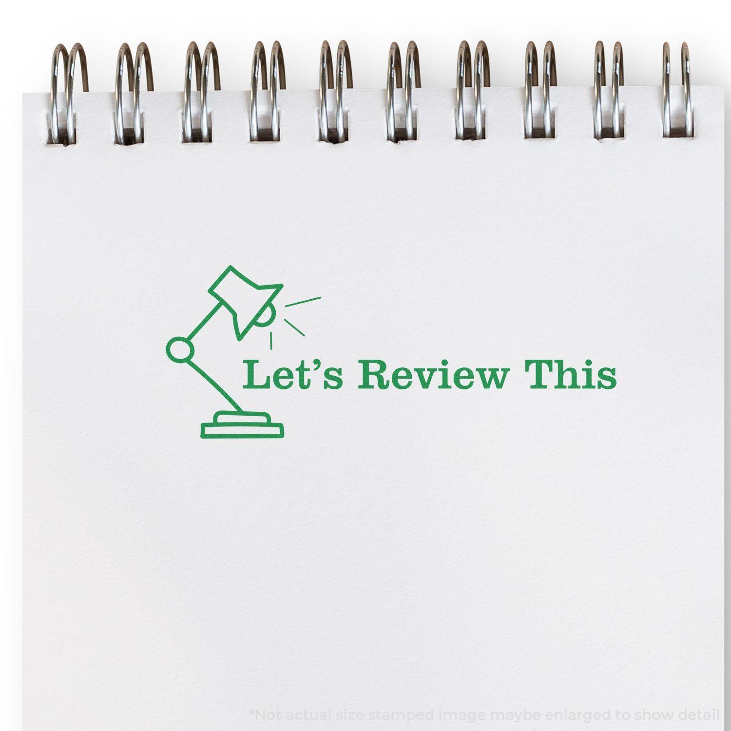 Large Lets Review This with Lamp Rubber Stamp in green ink on a white notepad, featuring a lamp icon and spiral binding at the top.