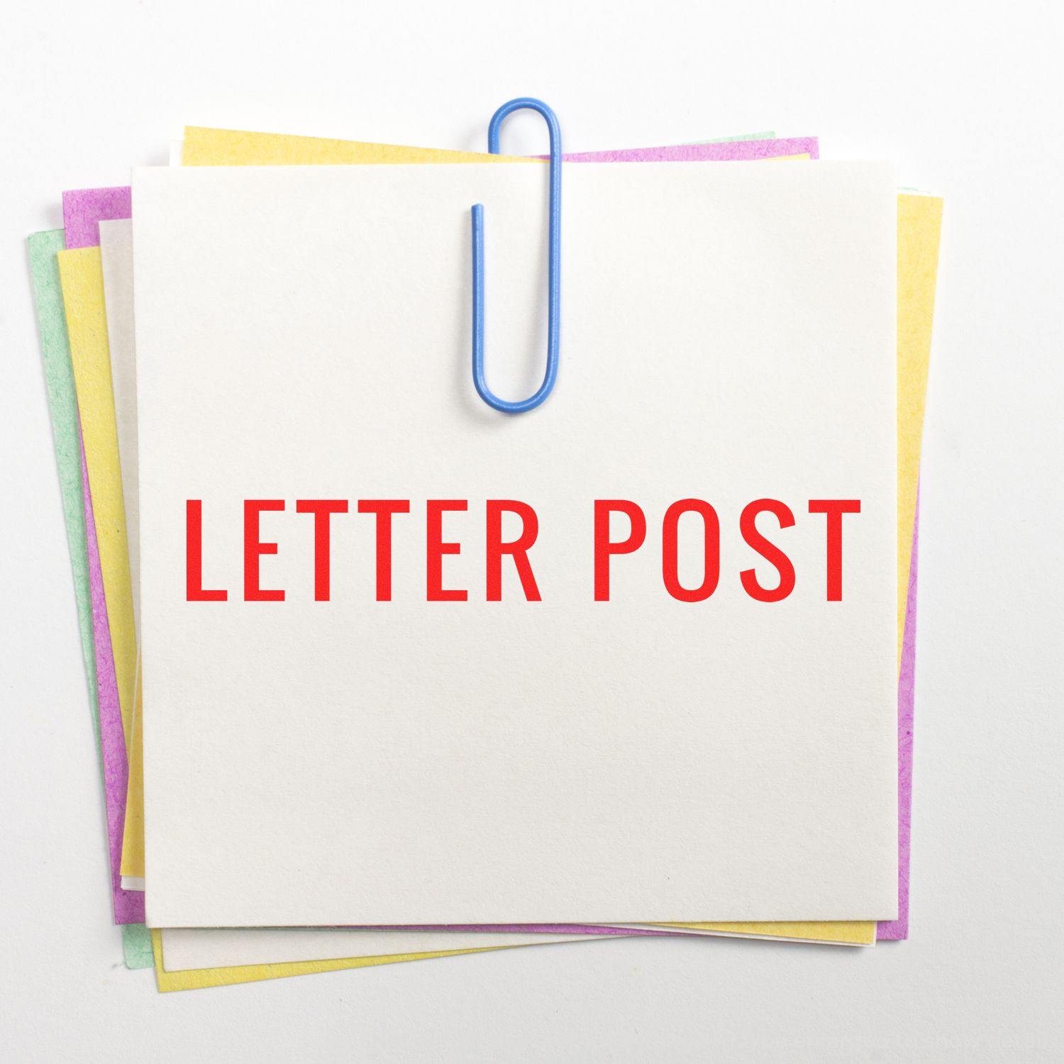 Large Letter Post Rubber Stamp impression on a white note, clipped with a blue paperclip, stacked on colorful papers.